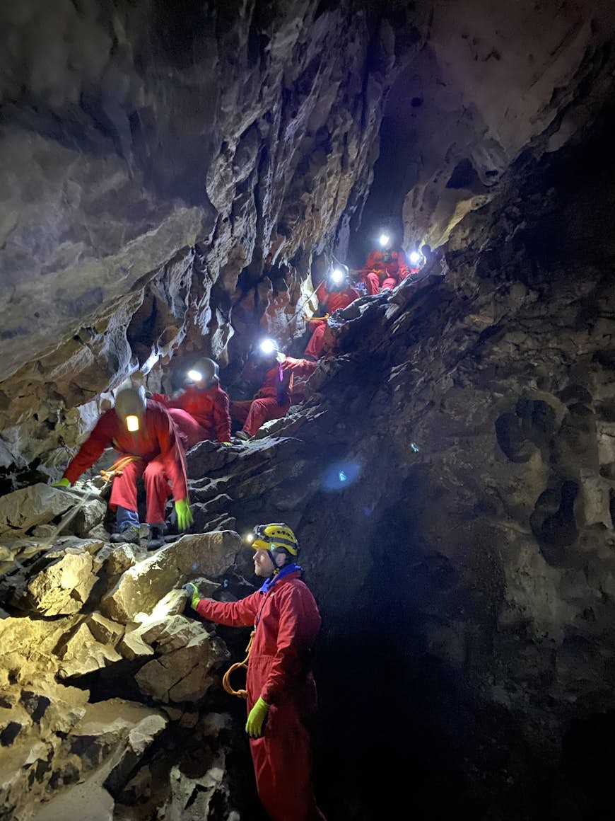 People in red jump suits with lantern helmets climb down a rocky trail in a cave during winter at Banff and Lake Louise