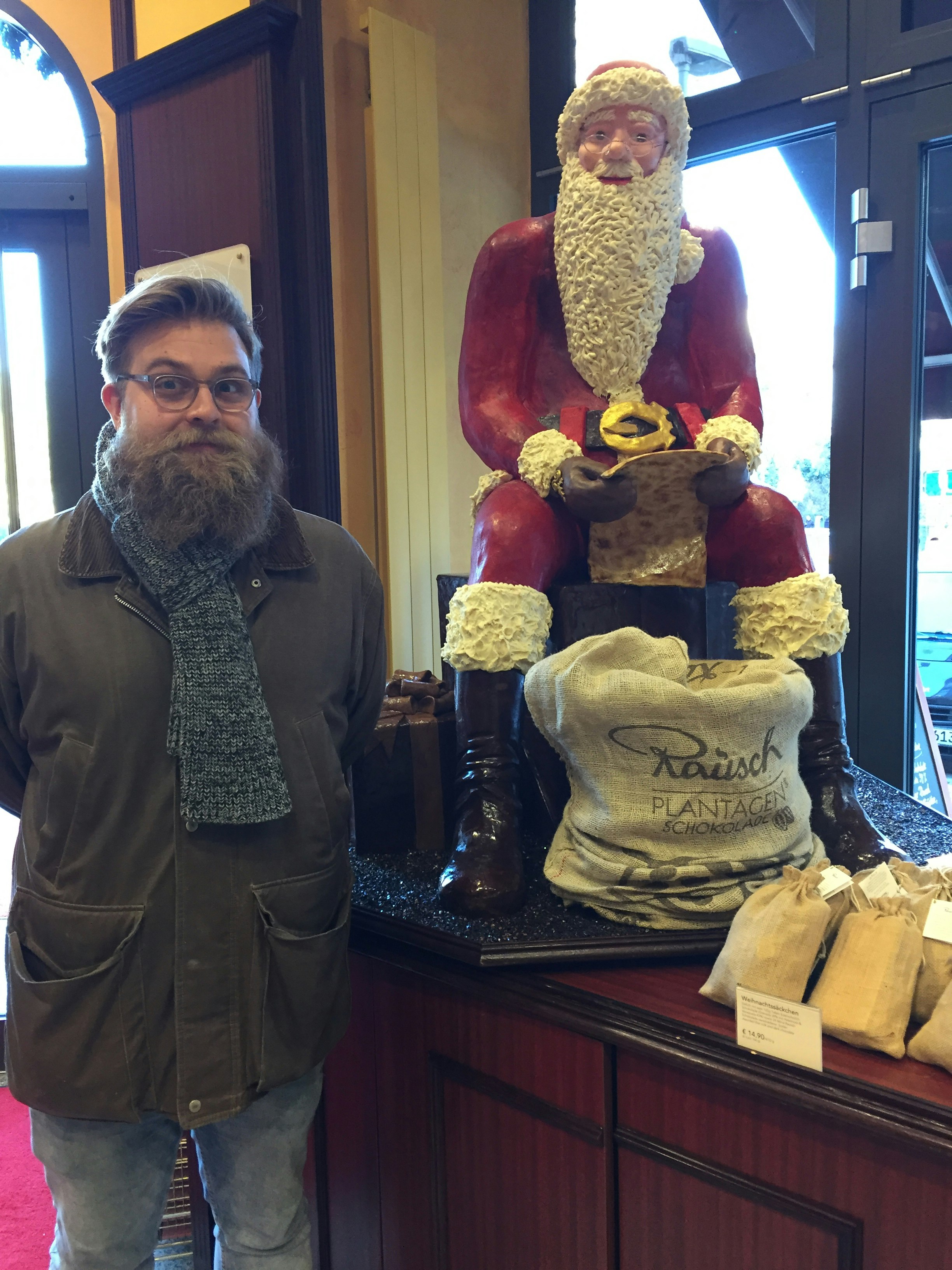 Writer Ryan Barrell is standing next to a sculpture of Santa Claus, made entirely out of chocolate, at Rausch Schokoladenhaus.