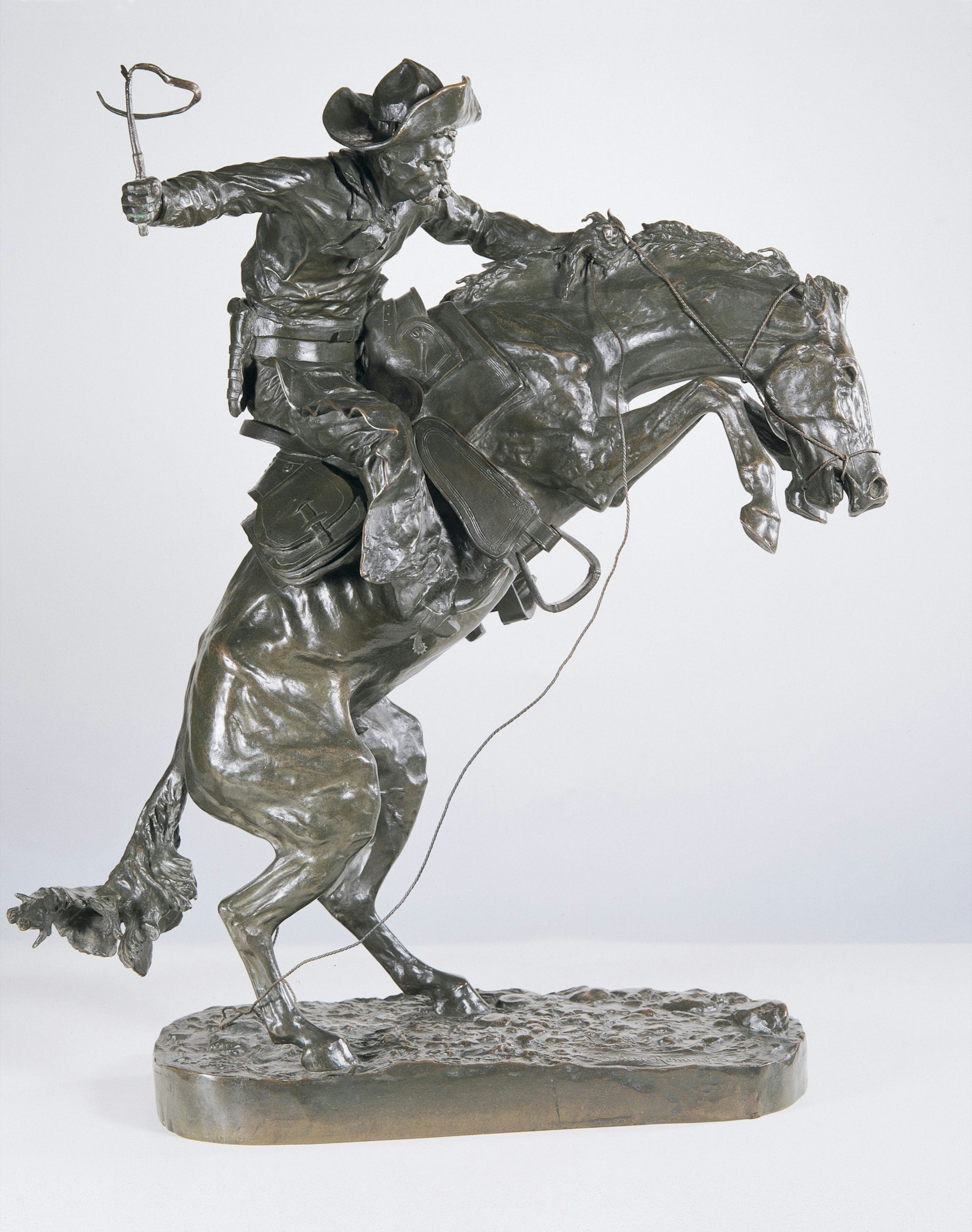 A bronze sculpture shows a cowboy riding a horse that is trying to violently throw him off in a very action-packed scene with wild contortions; Where to see Remington in America