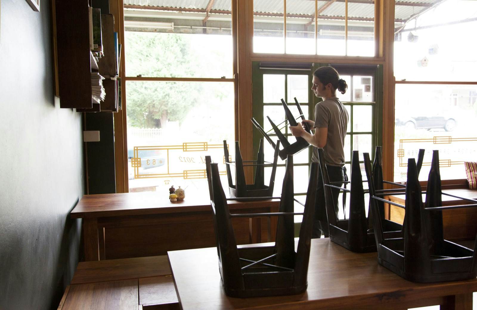 A waiter puts up stools on top of tables in a restaurant in broad daylight