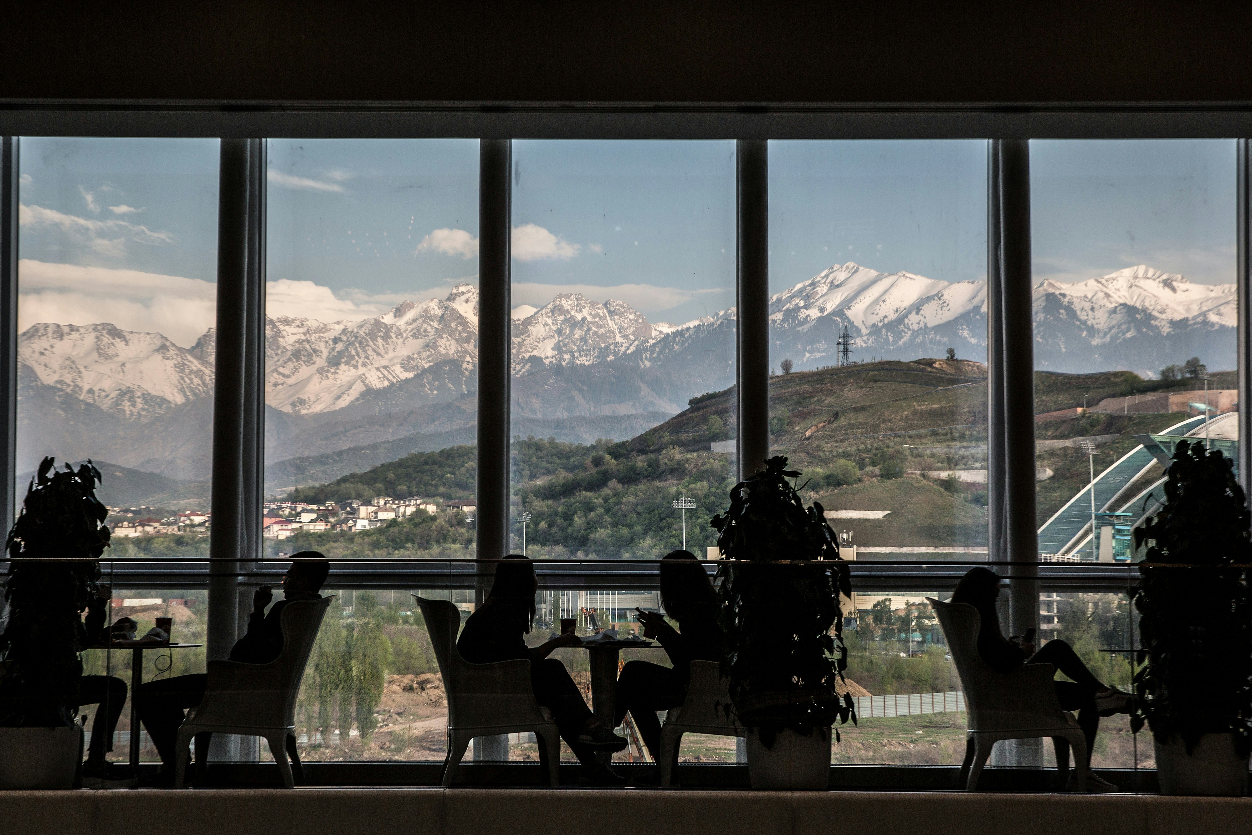 Kunderna är silhuetterade när de äter på en restaurang på Esentai Mall i Almaty, Kazakstan.  Genom de vägglånga fönstren syns stora berg.