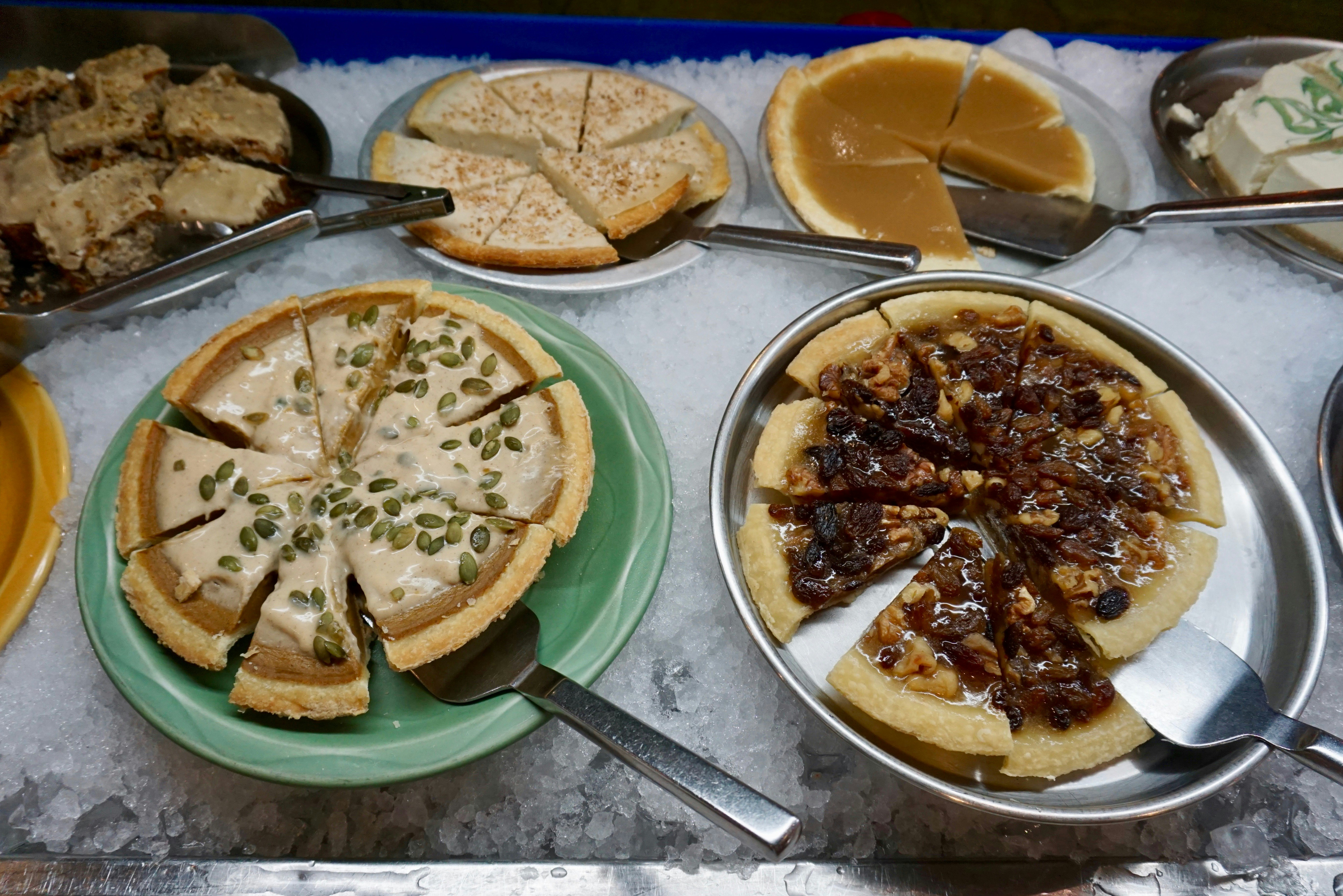 An arrangement of desserts such as pecan pie are sitting on stainless steel platters on a bed of crushed ice.