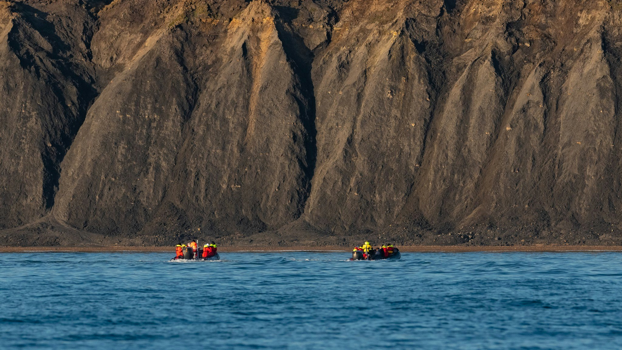 People in two inflatable explorer boats on the sea in front of cliffs 