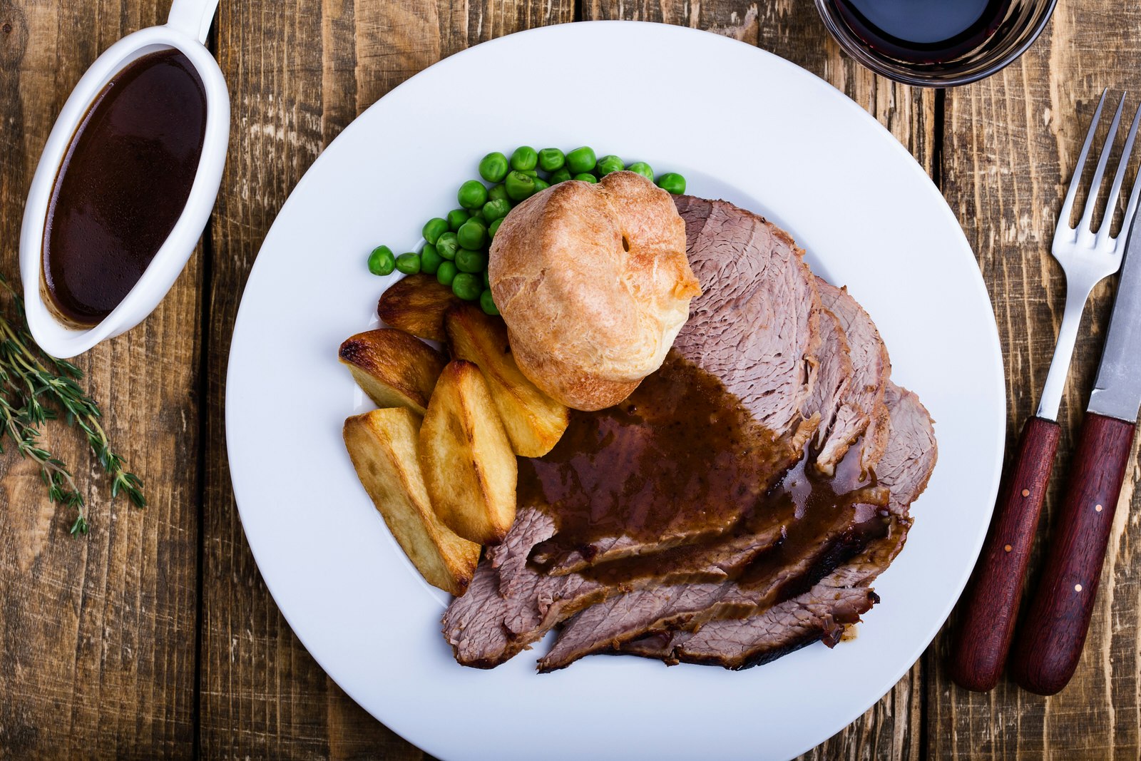 Sunday roast with roast beef, roast potatoes, green peas, Yorkshire pudding and gravy on a rustic wooden table viewed from above; a traditional British dish.