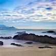 Looking across sands trapped between rocky outcrops on the beach of Robben Island; across the waters in the distance is Cape Town and the unmistakable flat-topped Table Mountain.
