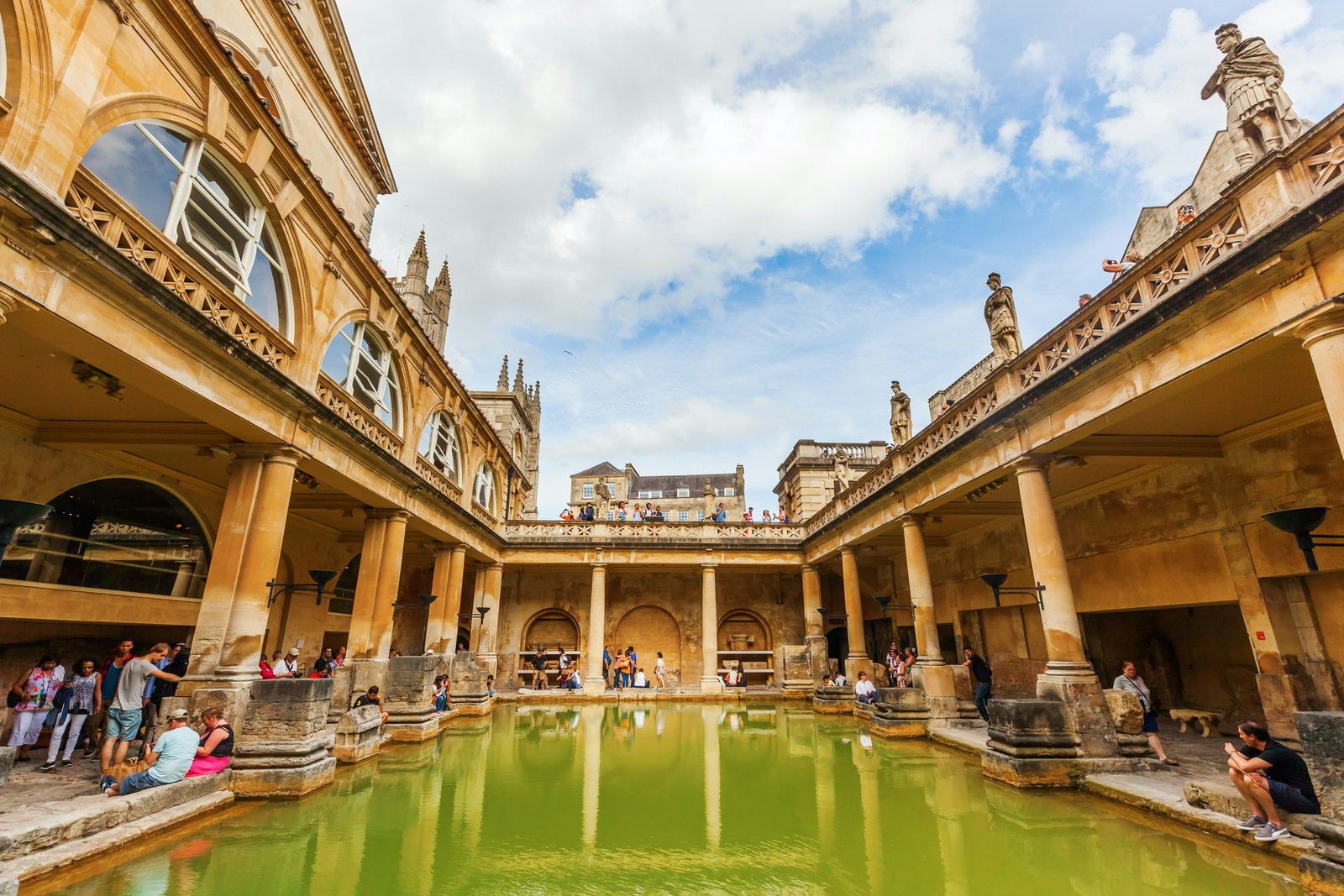 Roman baths interior under a cloudy sky.