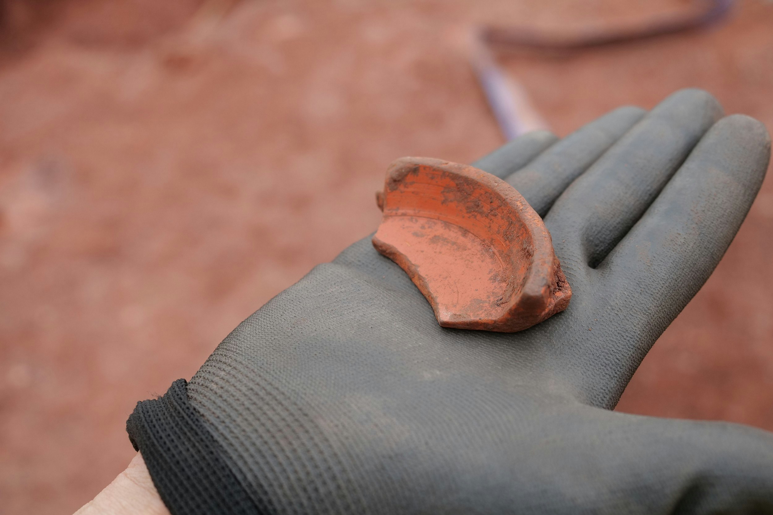 A gloved hand holding a pottery fragment discovered in the remains of a Roman fort.