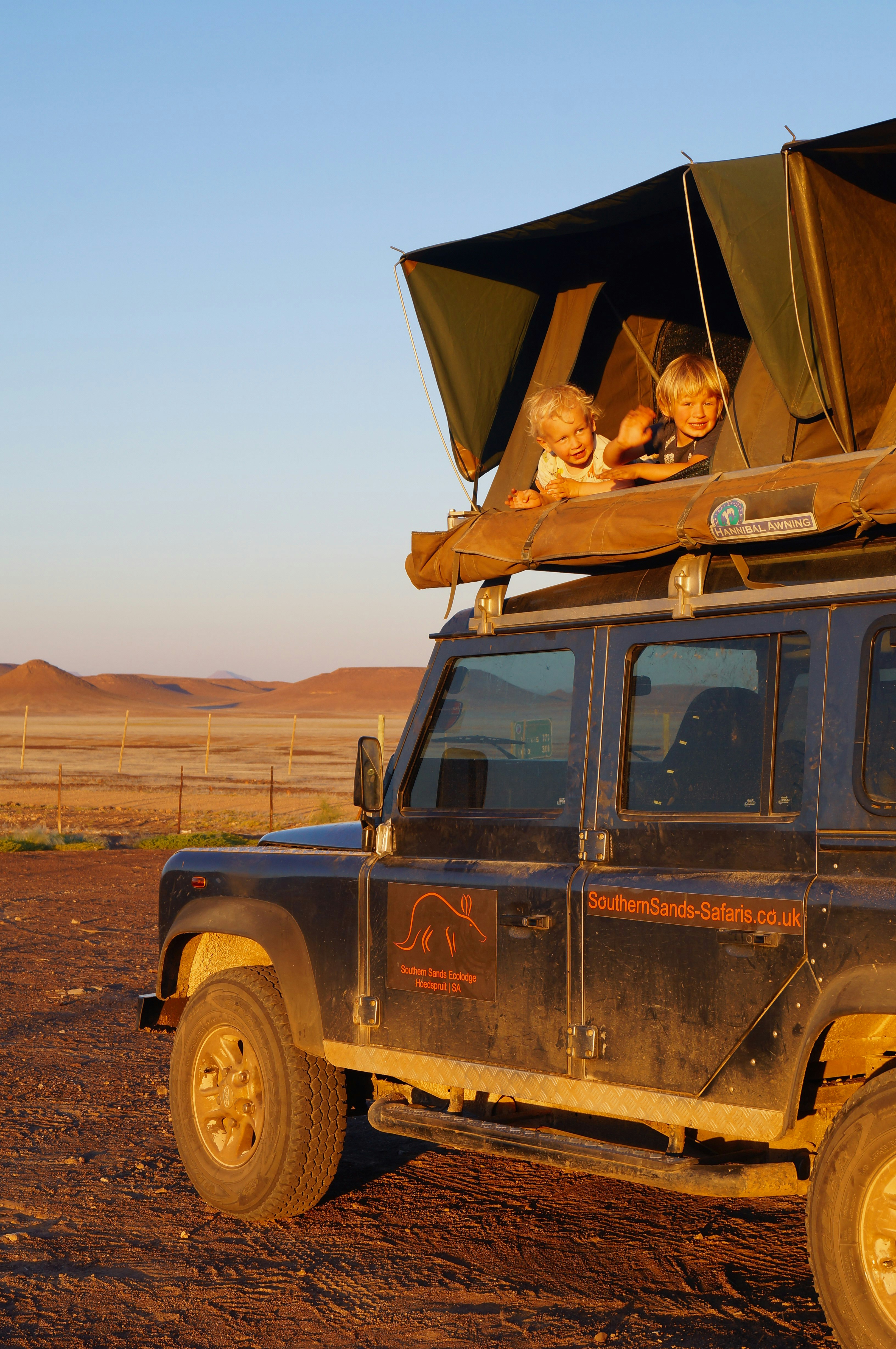 Two small boys sit in a rooftop tent atop a 4WD vehicle.