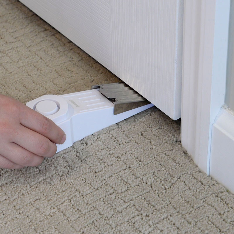 A person is inserting the SABRE door stop alarm under a door in a room.