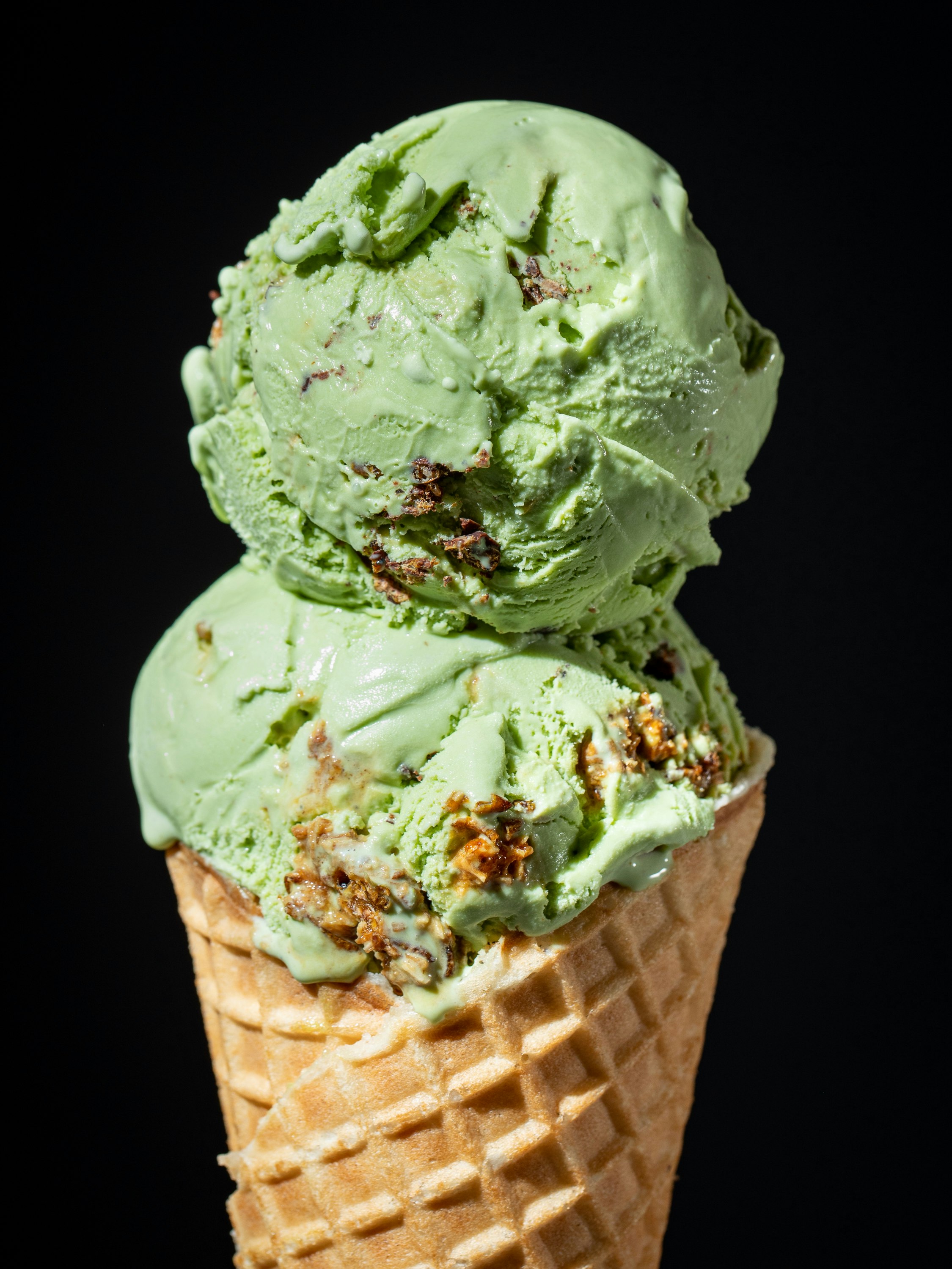 Two scoops of green-colored ice cream on a waffle cone. If you look closely, you can see chunks of chocolate-covered crickets.