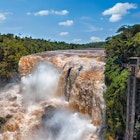 Brown colored water rushes over a tall falls in near the city of Ciudad del Este in Paraguay