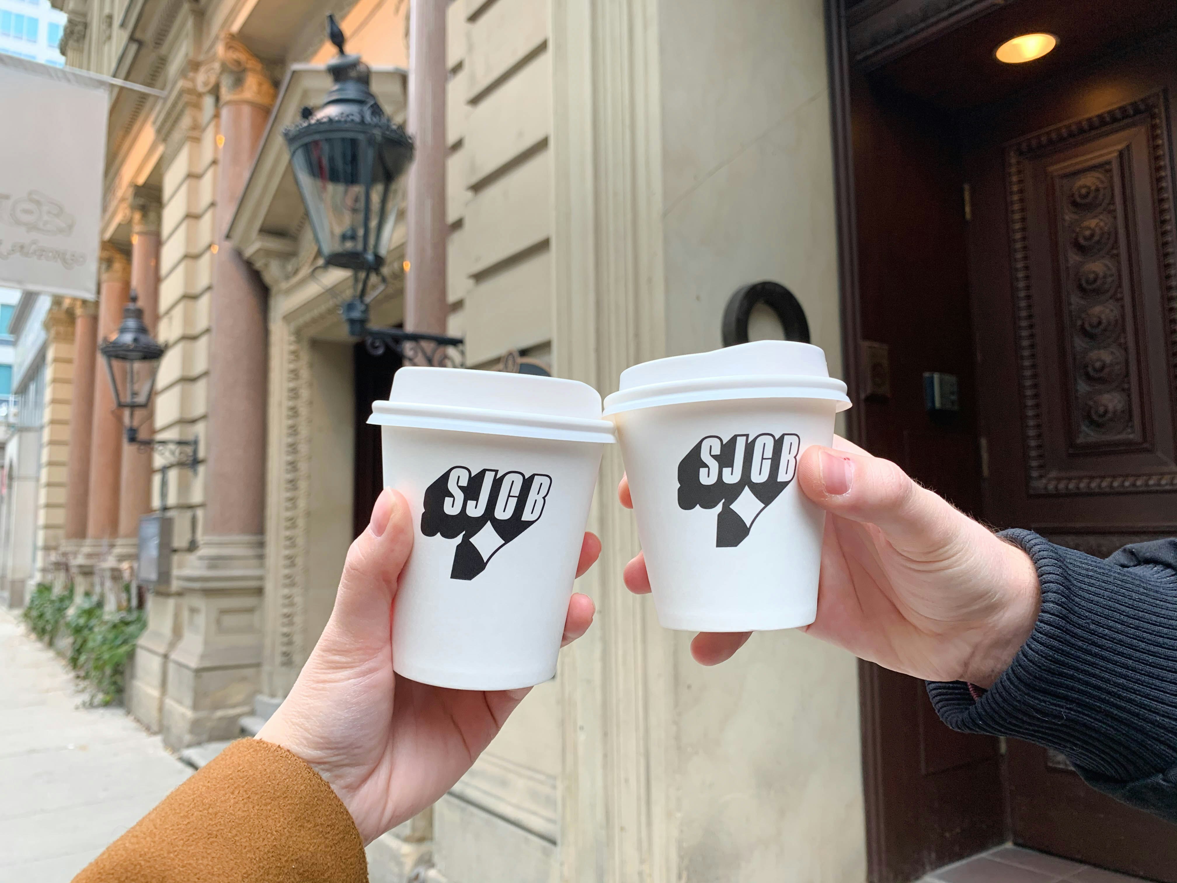Two hands hold up cups of artisinal coffee. 