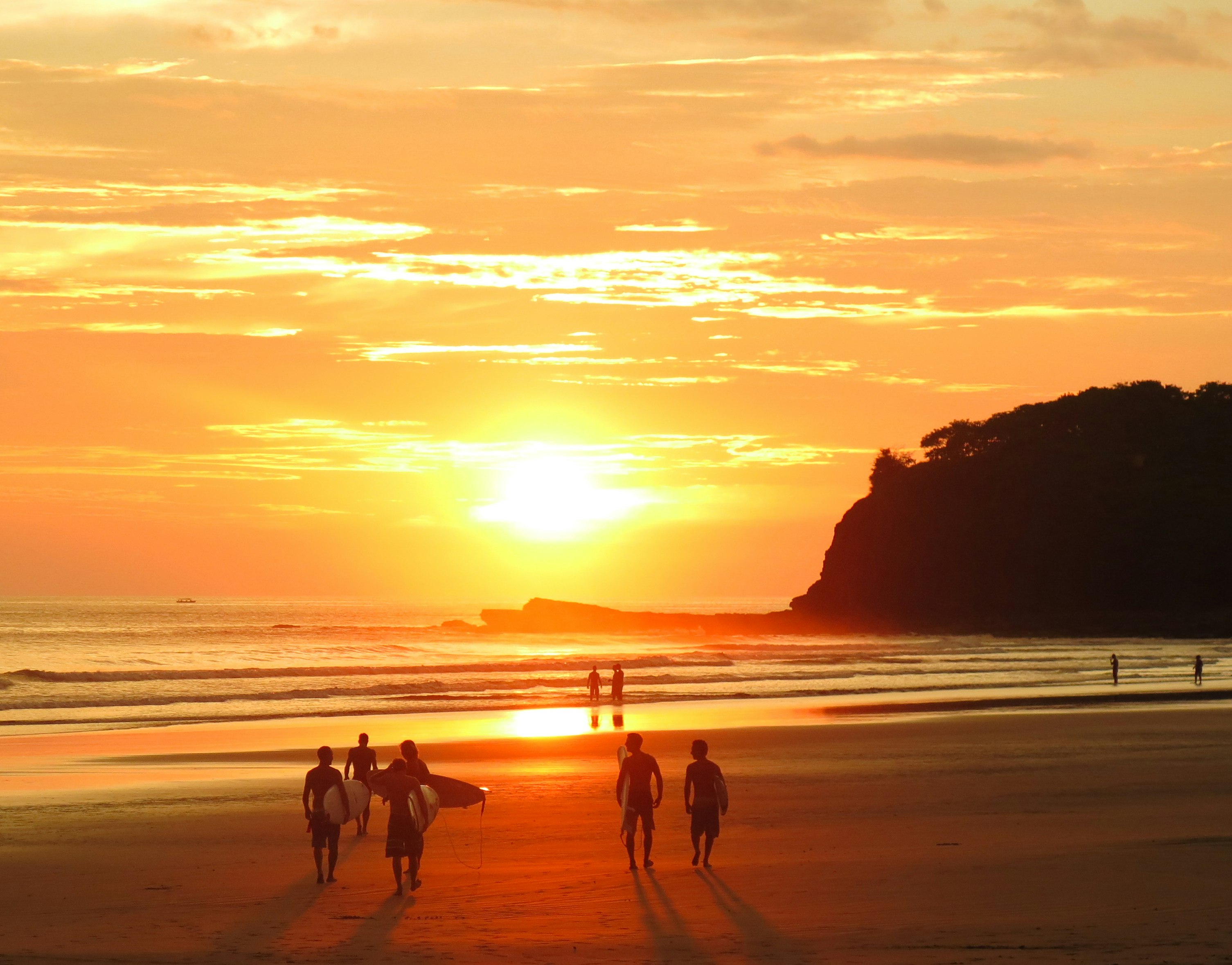 A group of surfers holding surf boards walk toward the water as sun creates a golden glow on the water and the sand; Nicaragua best beaches