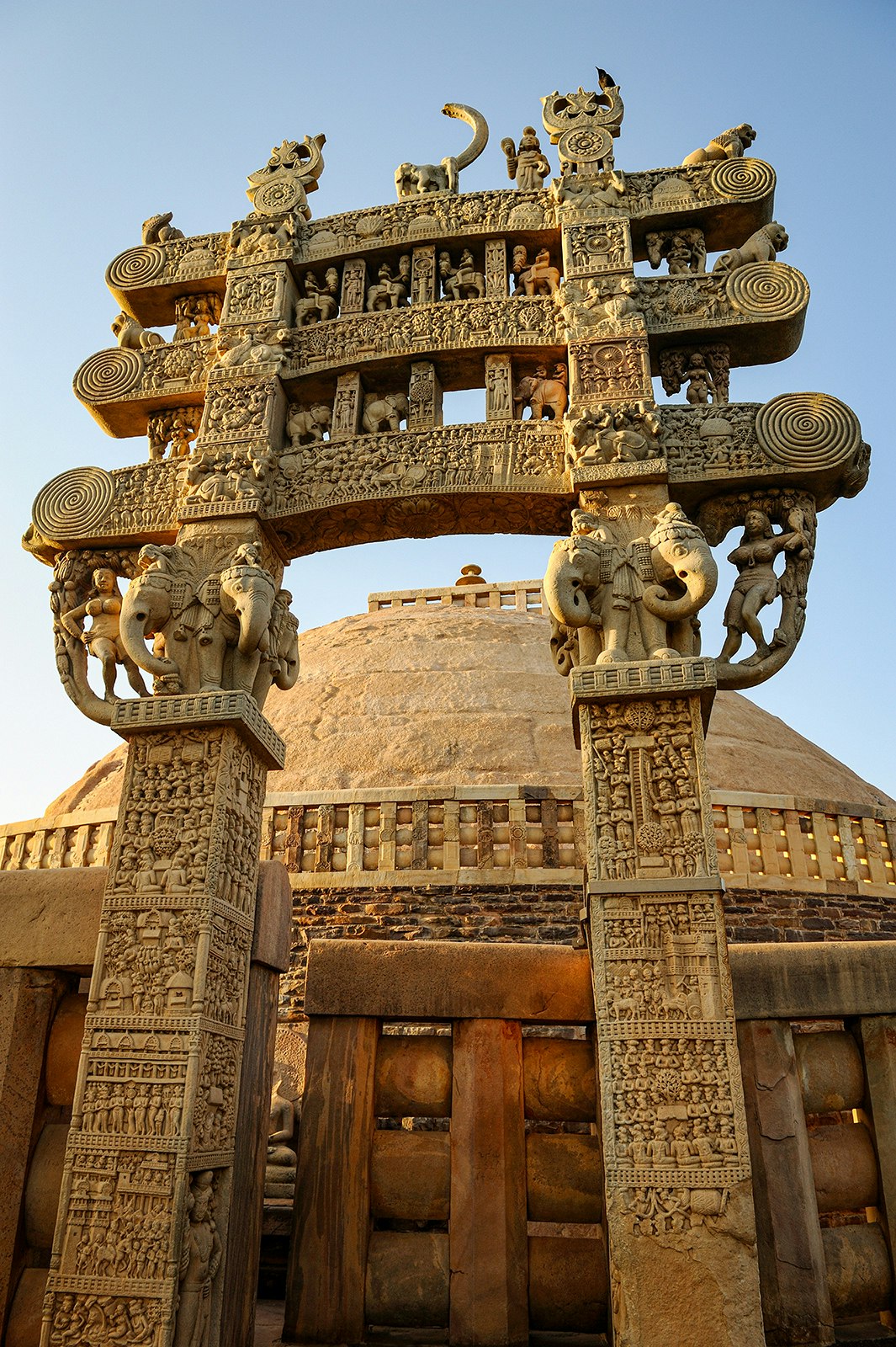 An intricately carved gate sits in front of the rounded Great Stupa in Sanchi, India.