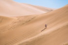 Wide shot of a man sandboarding down a large dune in Peru