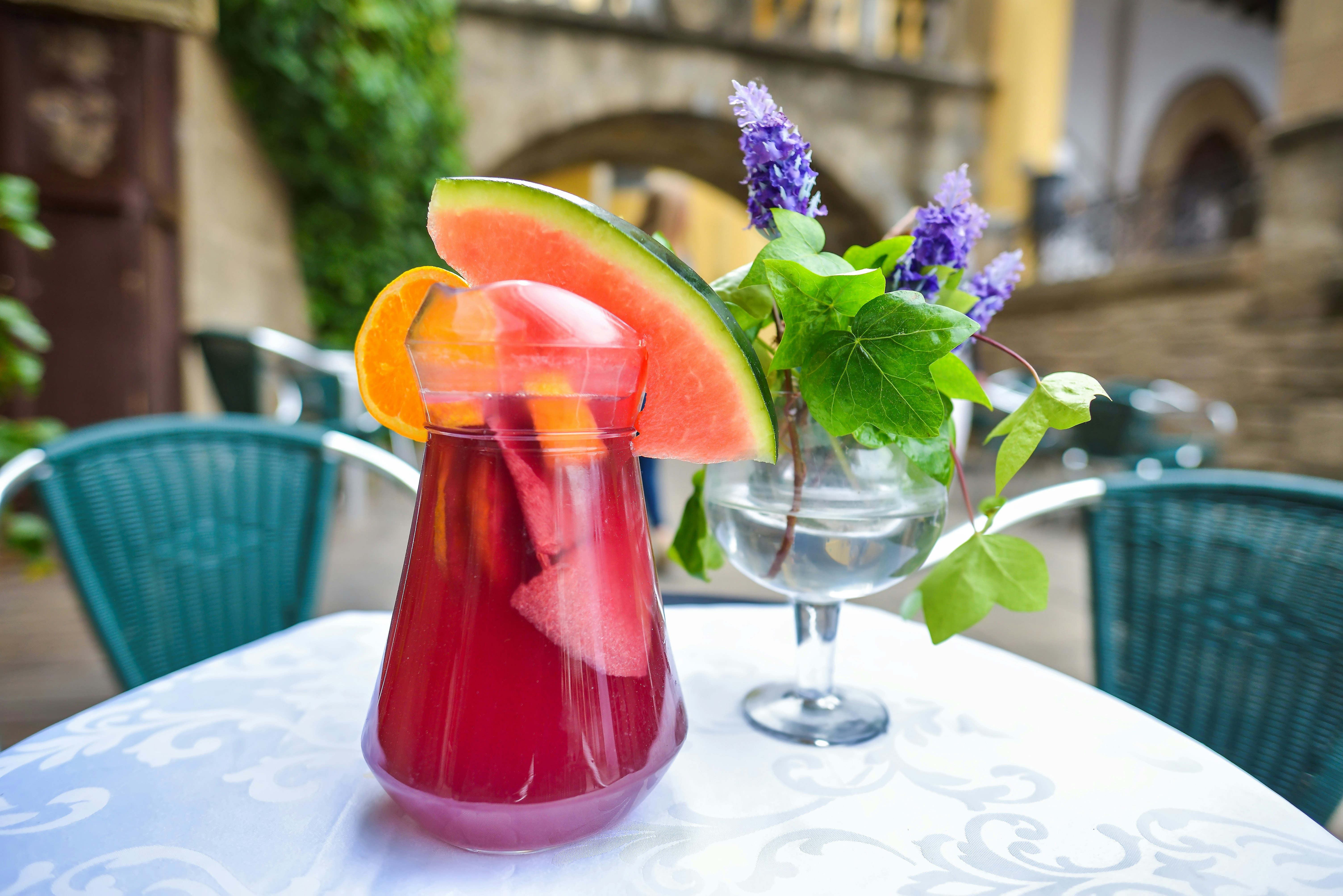 A large glass of ruby-colored Sangria. A large wedge of watermelon and orange slice hang off the rim of the glass.