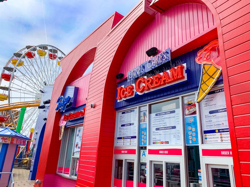 A multicolored ferris wheel is partially hidden by a large red-painted ice cream parlor in Santa Monica; California ice cream