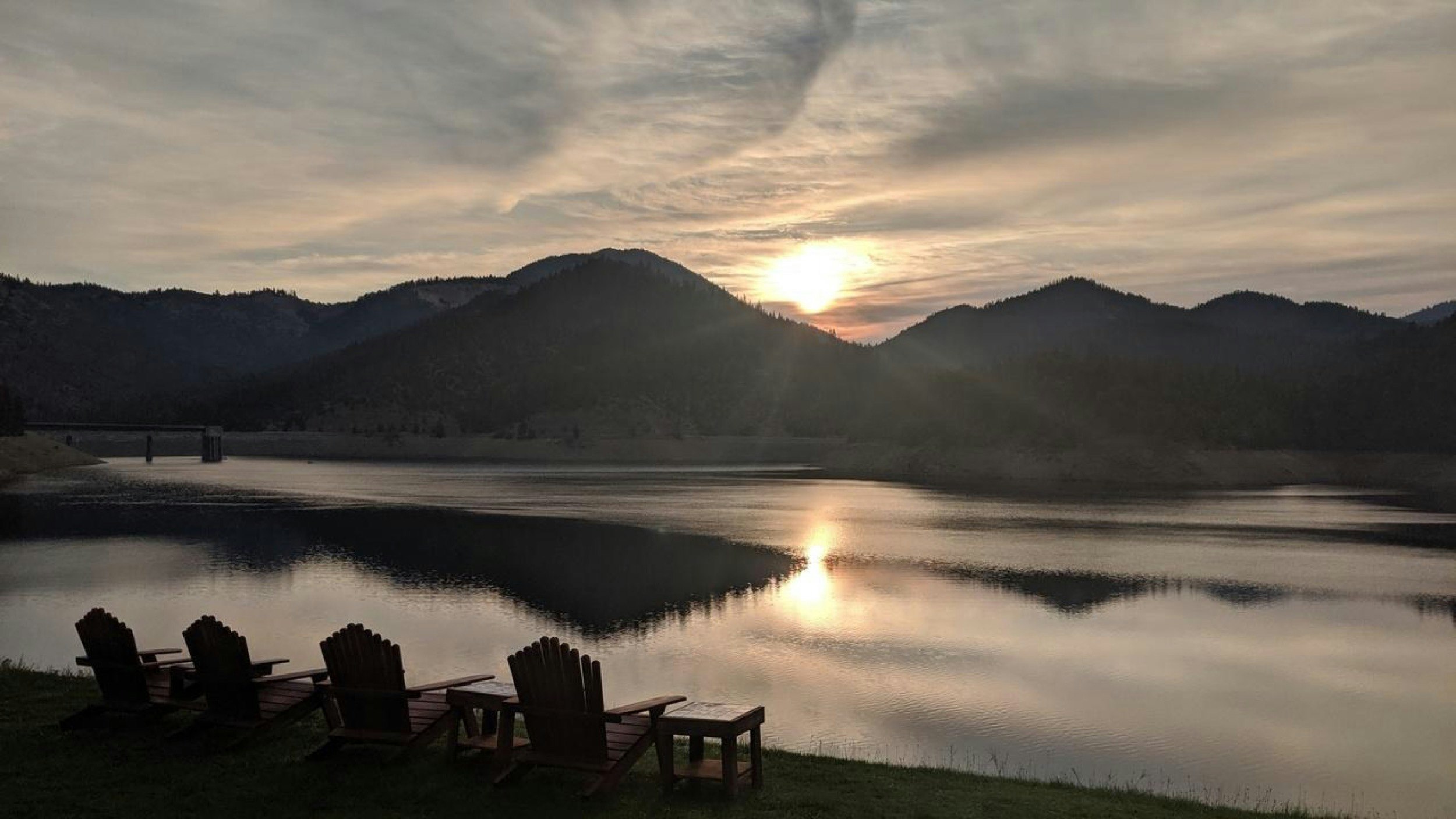 Adirondak chairs are set up next to a placid lake at the foot of a mountain at sunset in the Pacific Northwest