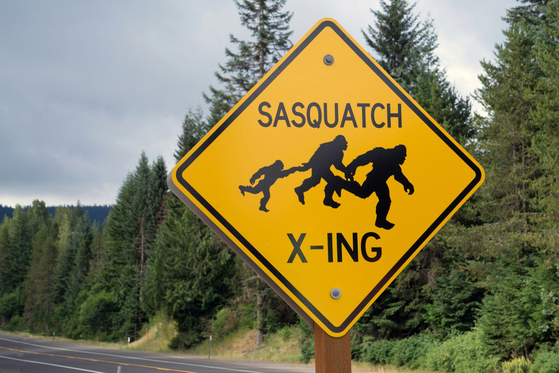 A road sign shows a family of three sasquatch running hand in hand with the words sasquatch crossing in Oregon