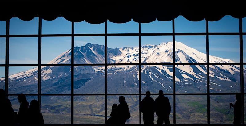 People stand in front of a large window looking out at the destroyed cone of Mt St Helens in Washington