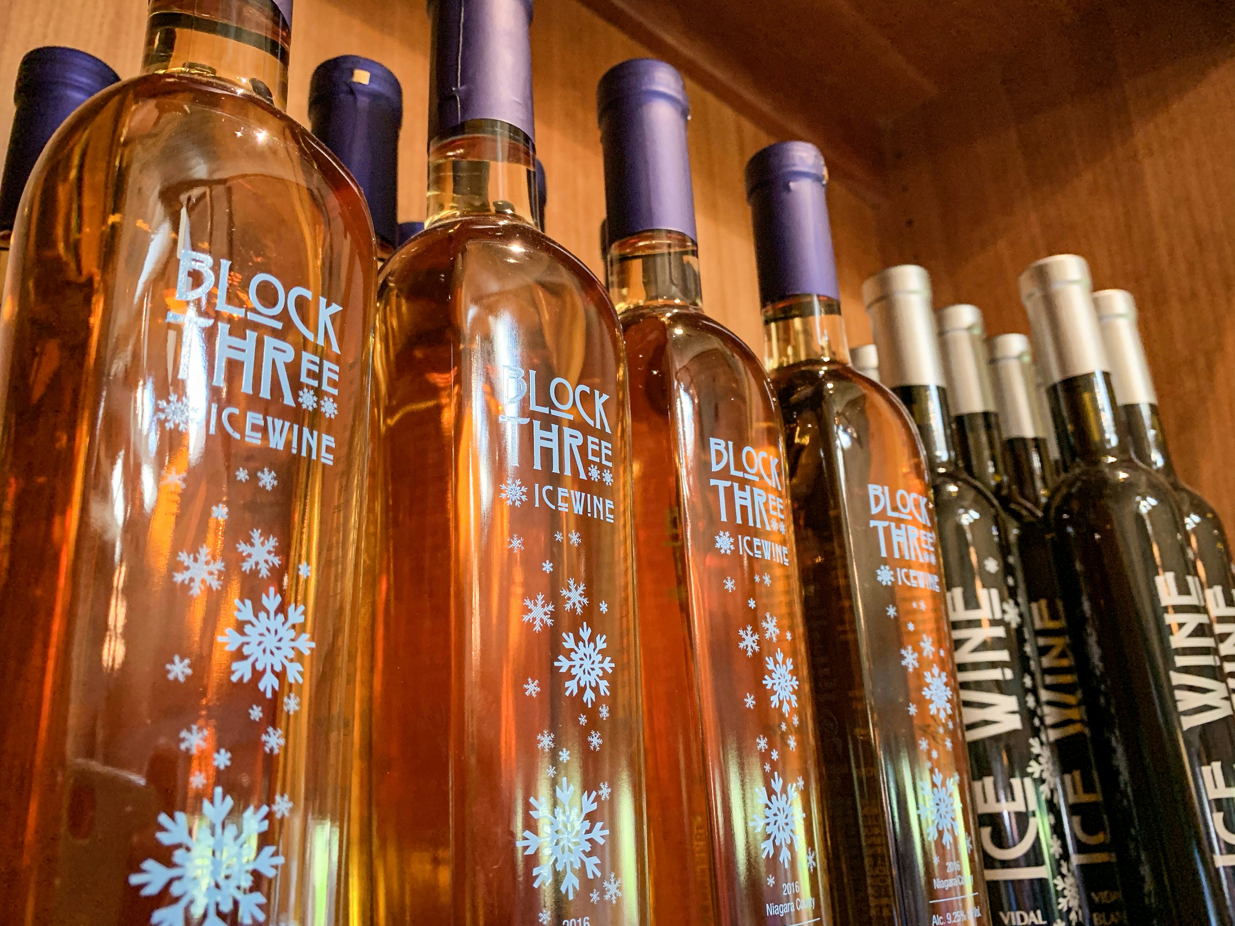 A collection of block three ice wine bottles sit on a wooden shelf 