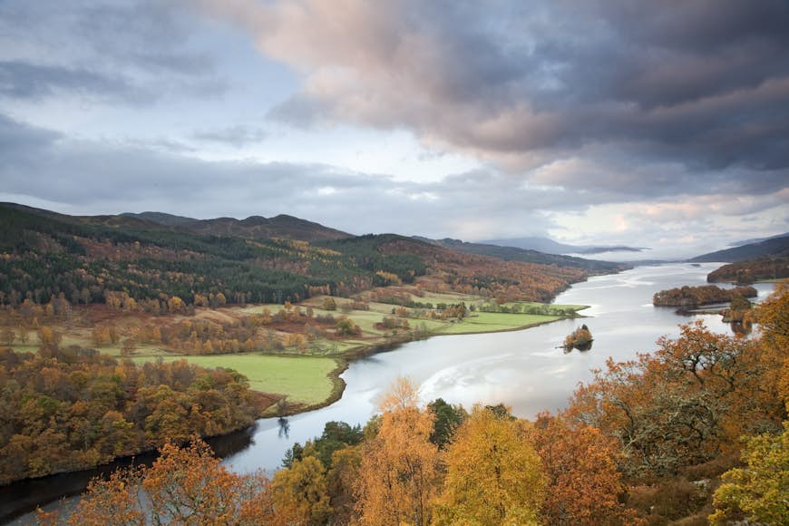 A Scottish loch near Pitlochry is framed by rolling farmland and hills covered in a mixture of green and autumn-colored leaves