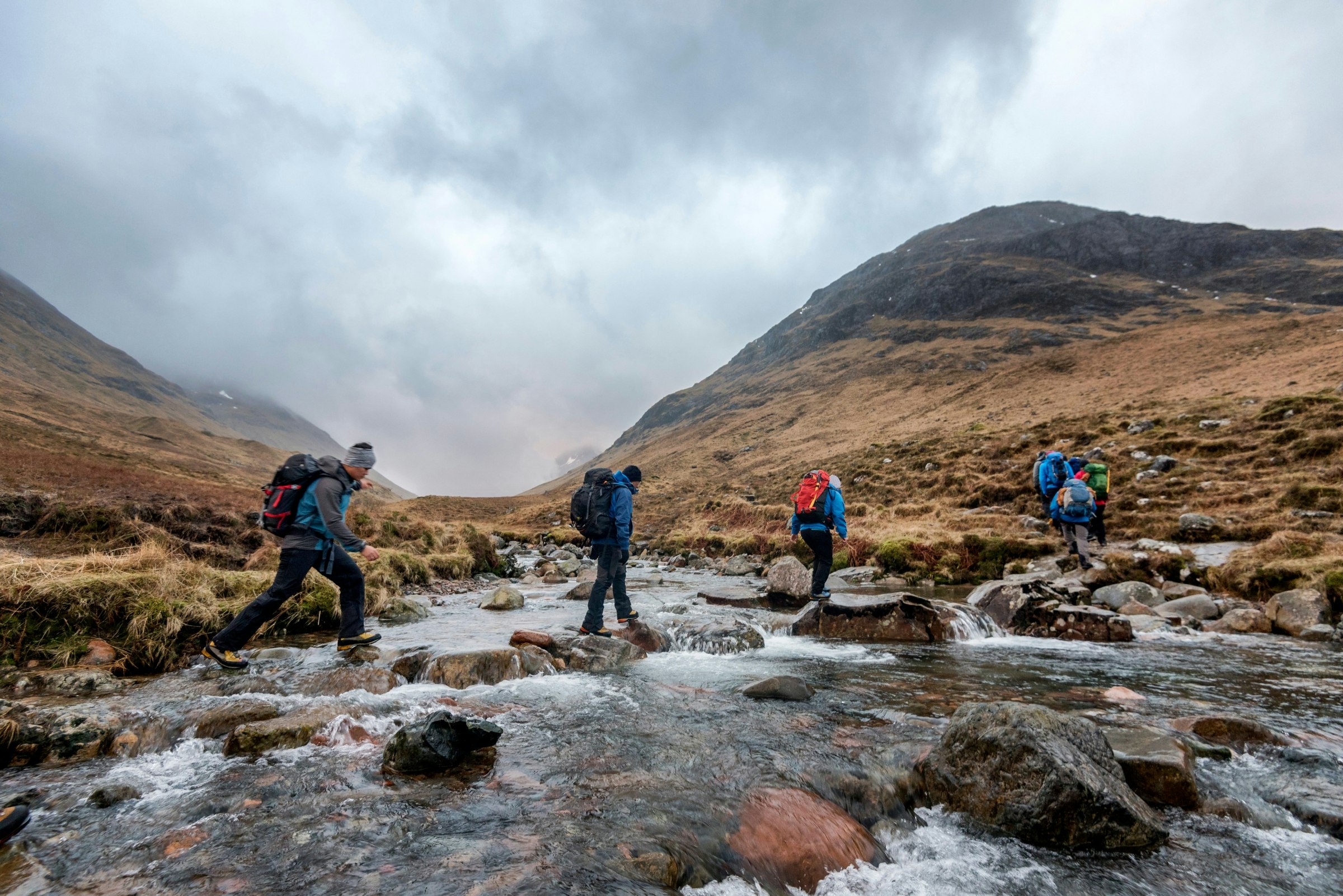 A trekking group crossing a stream on the Sron na Lairig route