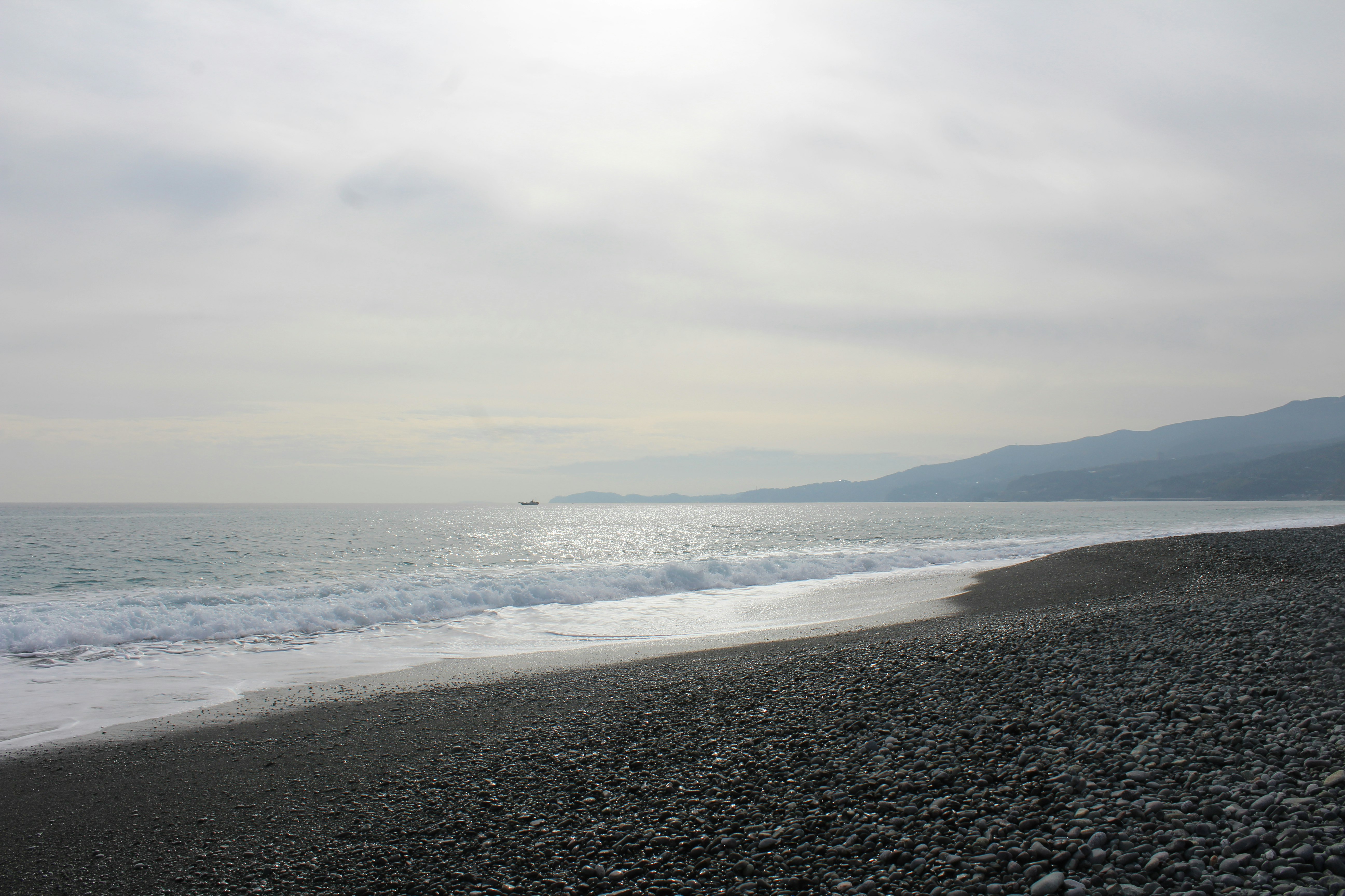 An overcast sky overlooks waves breaking on a rocky shore in Odawara