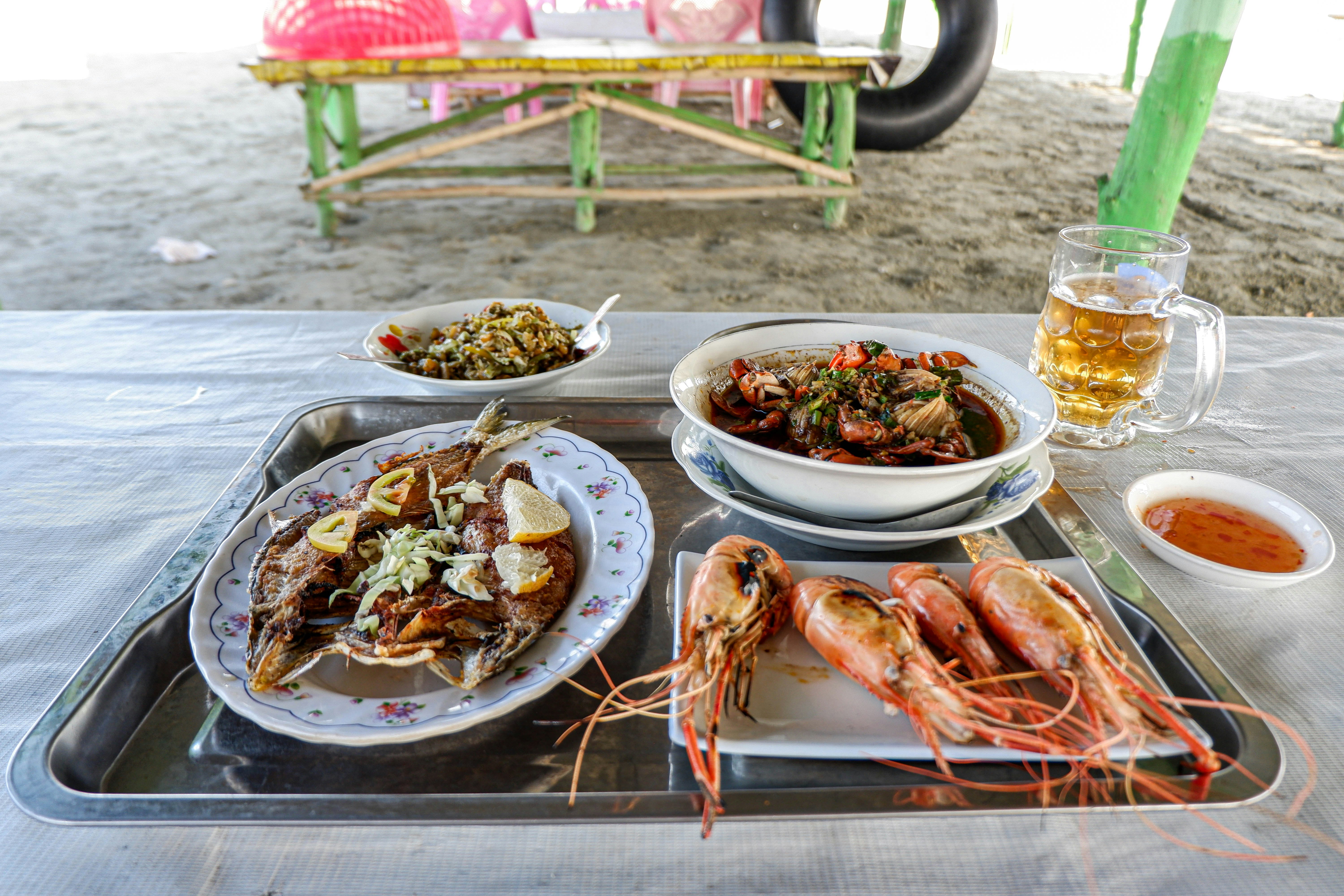 A tray of several seafood dishes - including fresh prawns and a crab curry - sits on a table on the sands of Ale-Wa beach.
