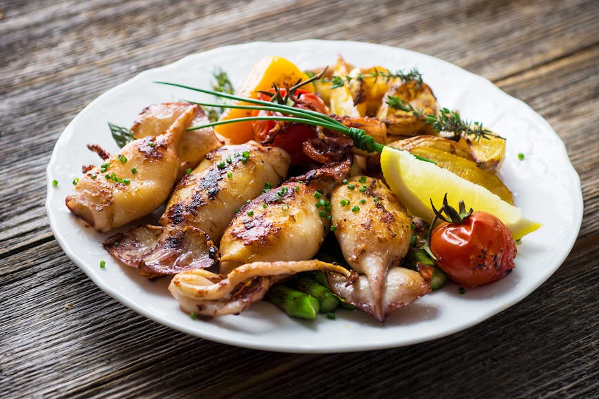 Grilled squid on a plate with lemon, tomato and asparagus