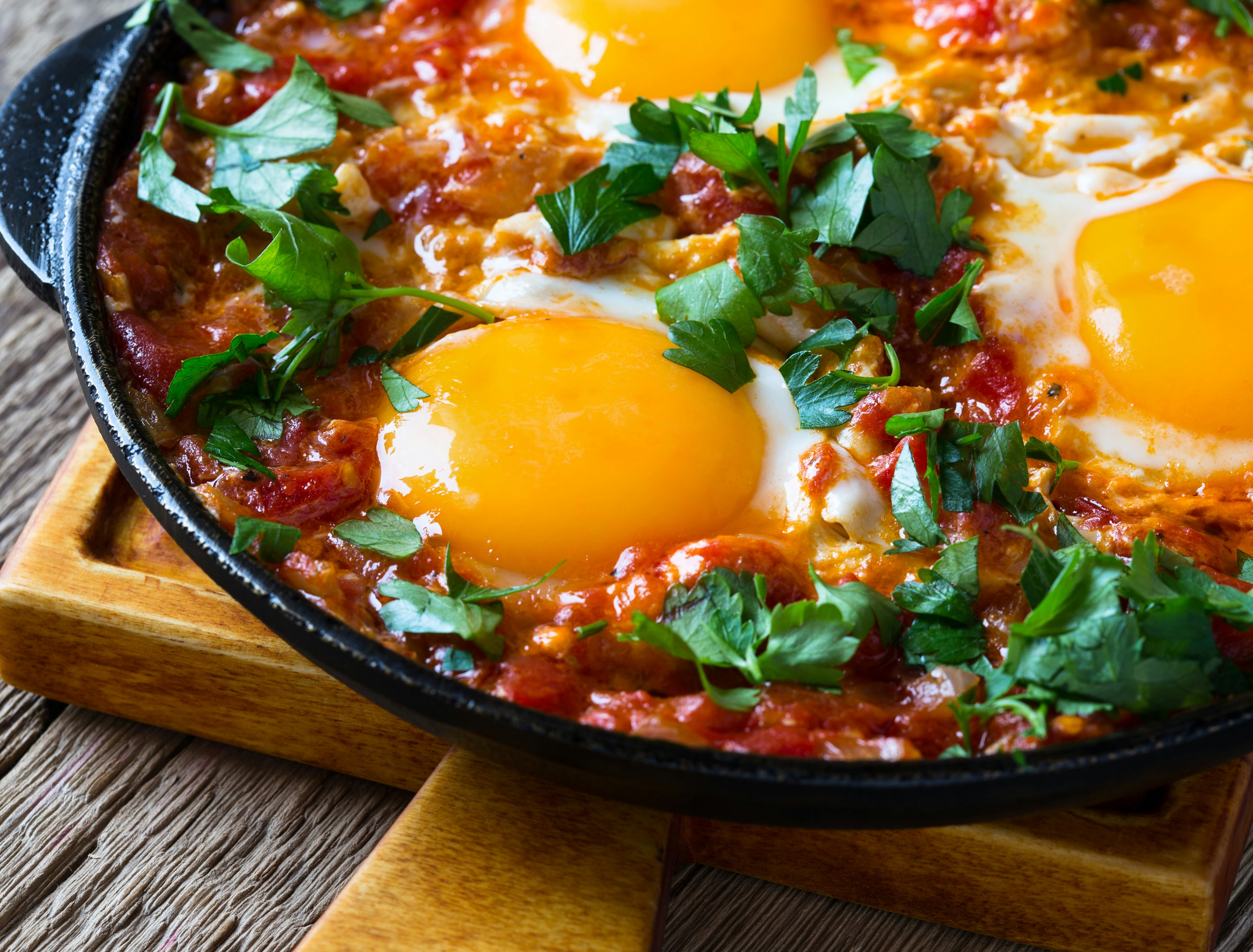 En närbild av shakshouka i en stor svart panna.  De gula äggulorna sticker ut mot rättens röda sås.