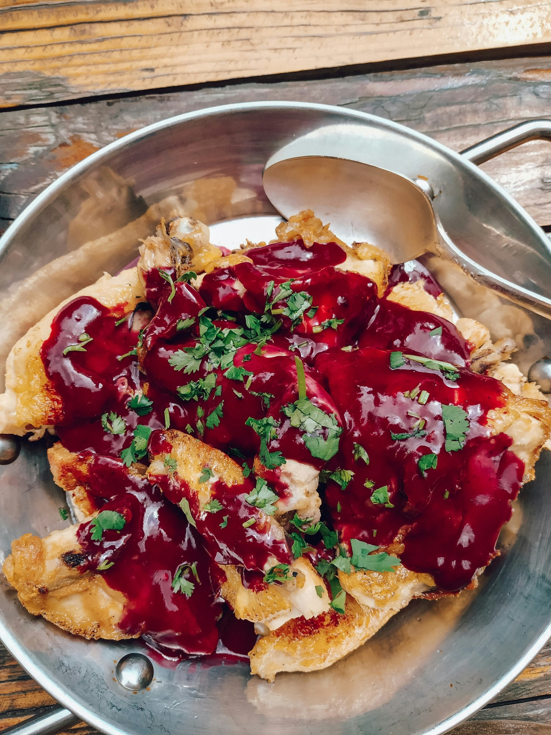 A close-up shot of fried chicken smothered in a red sauce and topped with chopped herbs