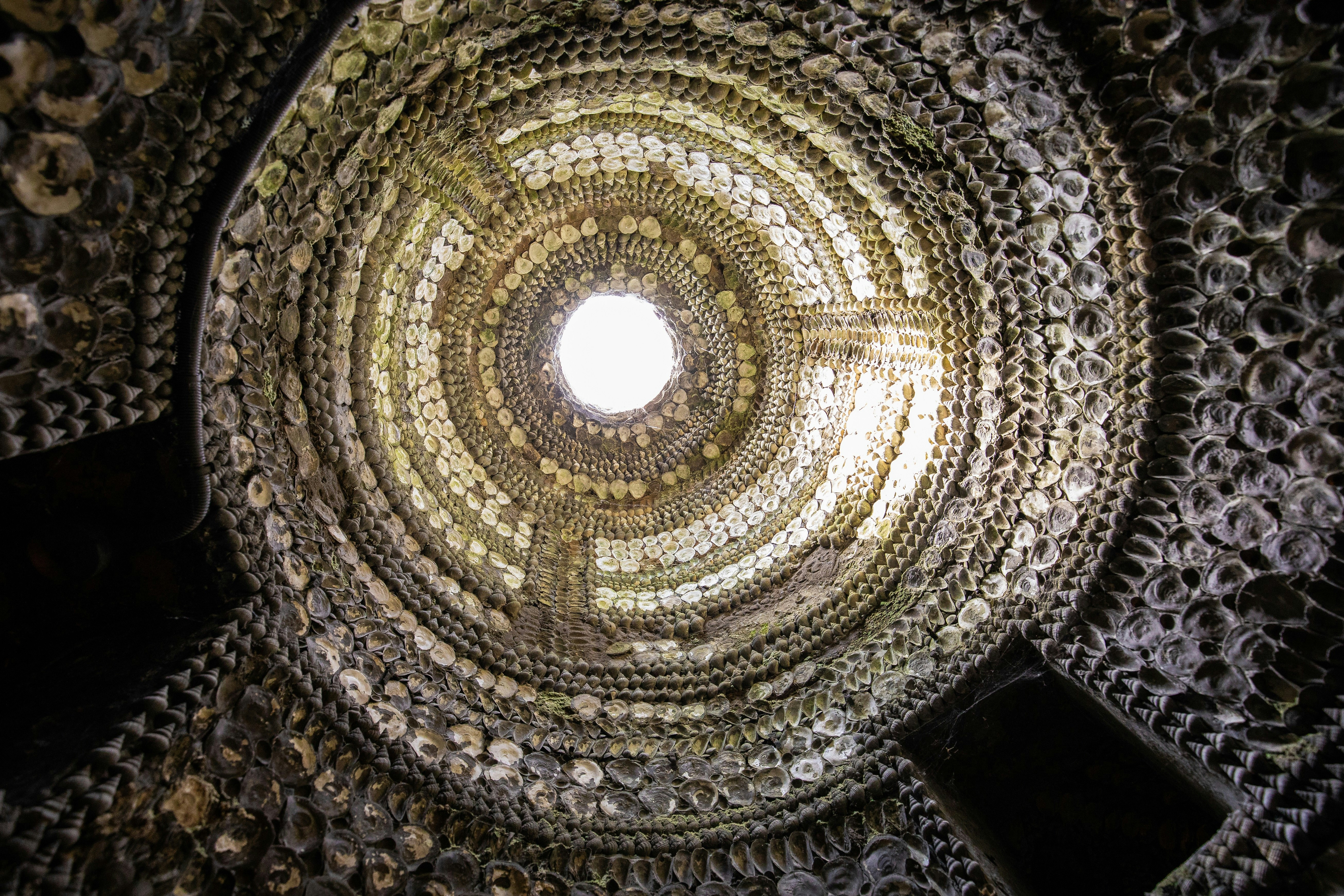 Looking up at an intricate shell-encrusted, domed ceiling in the Shell Grotto, Margate, with light appearing through a window at the top.