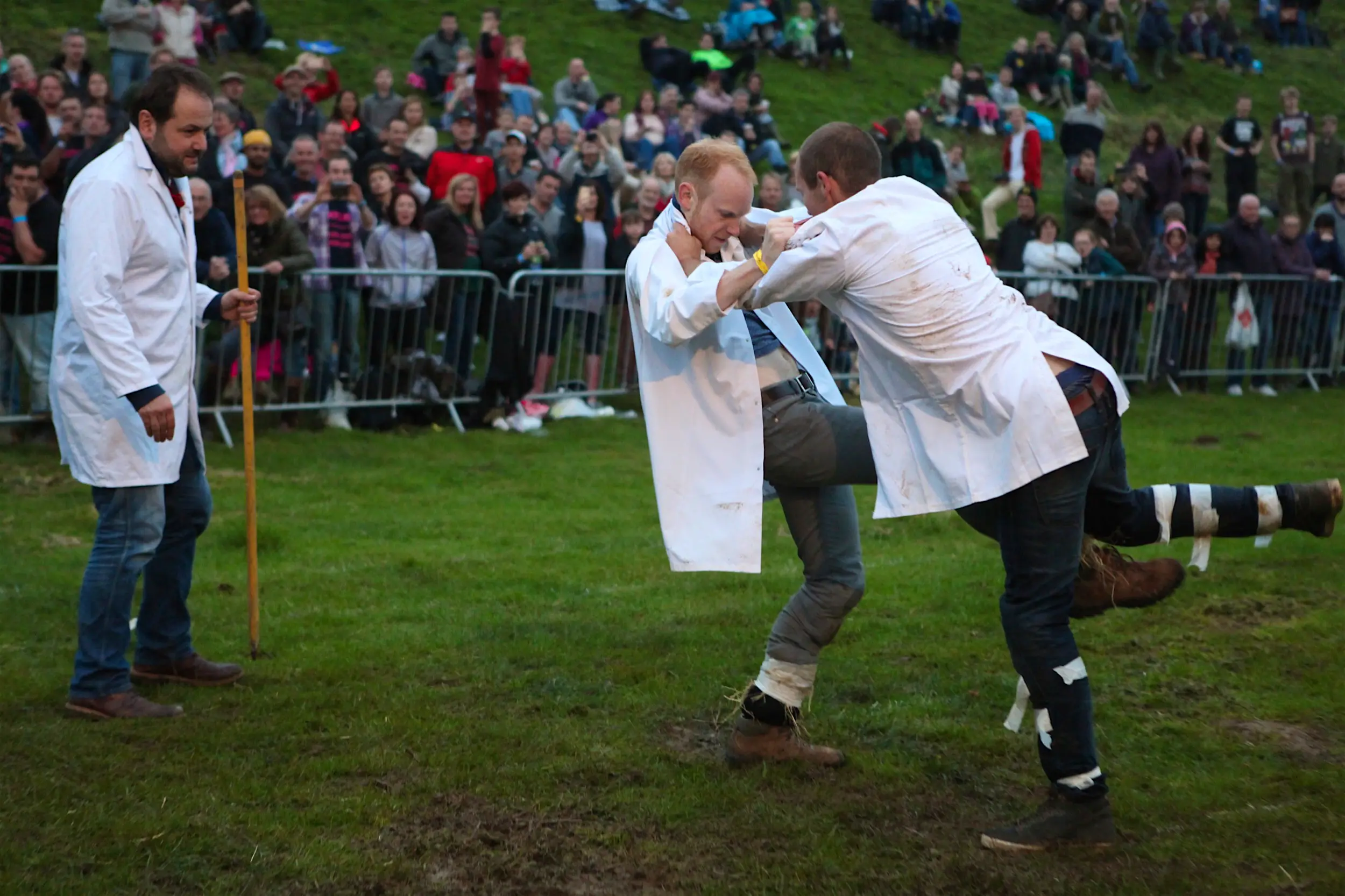 Shin_Kicking.jpg Two men are tangled up while trying to kick each others' shins under the watchful eye of a referee and observers; unique sporting events