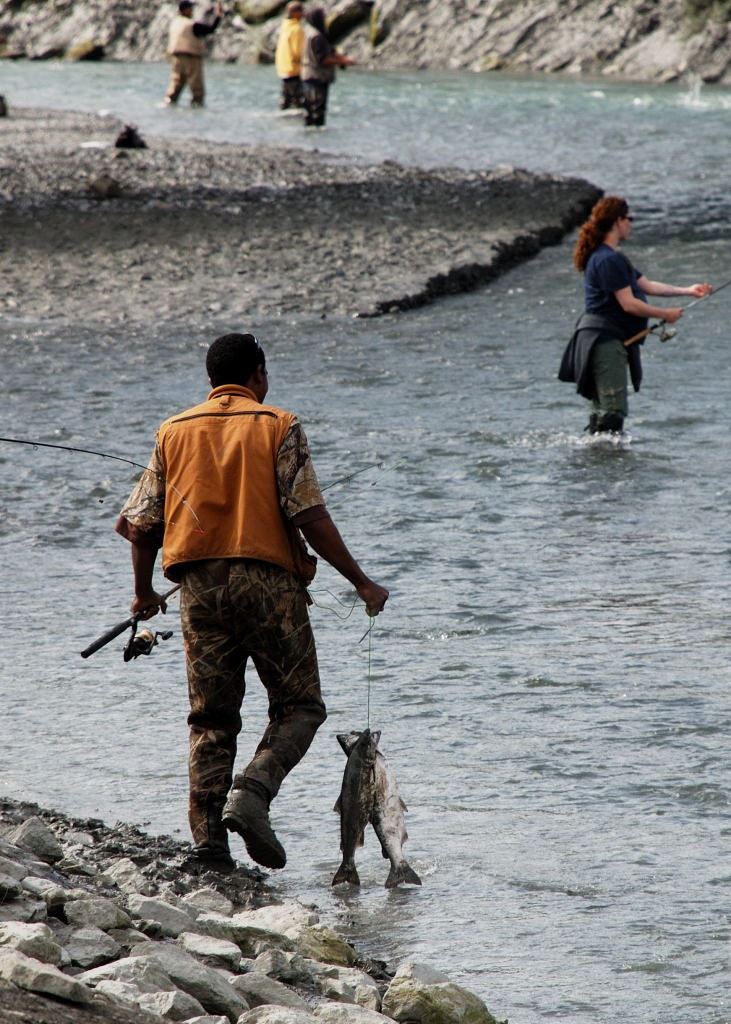 A fisherman carrying two freshly caught salmon on a fishing line near a creek