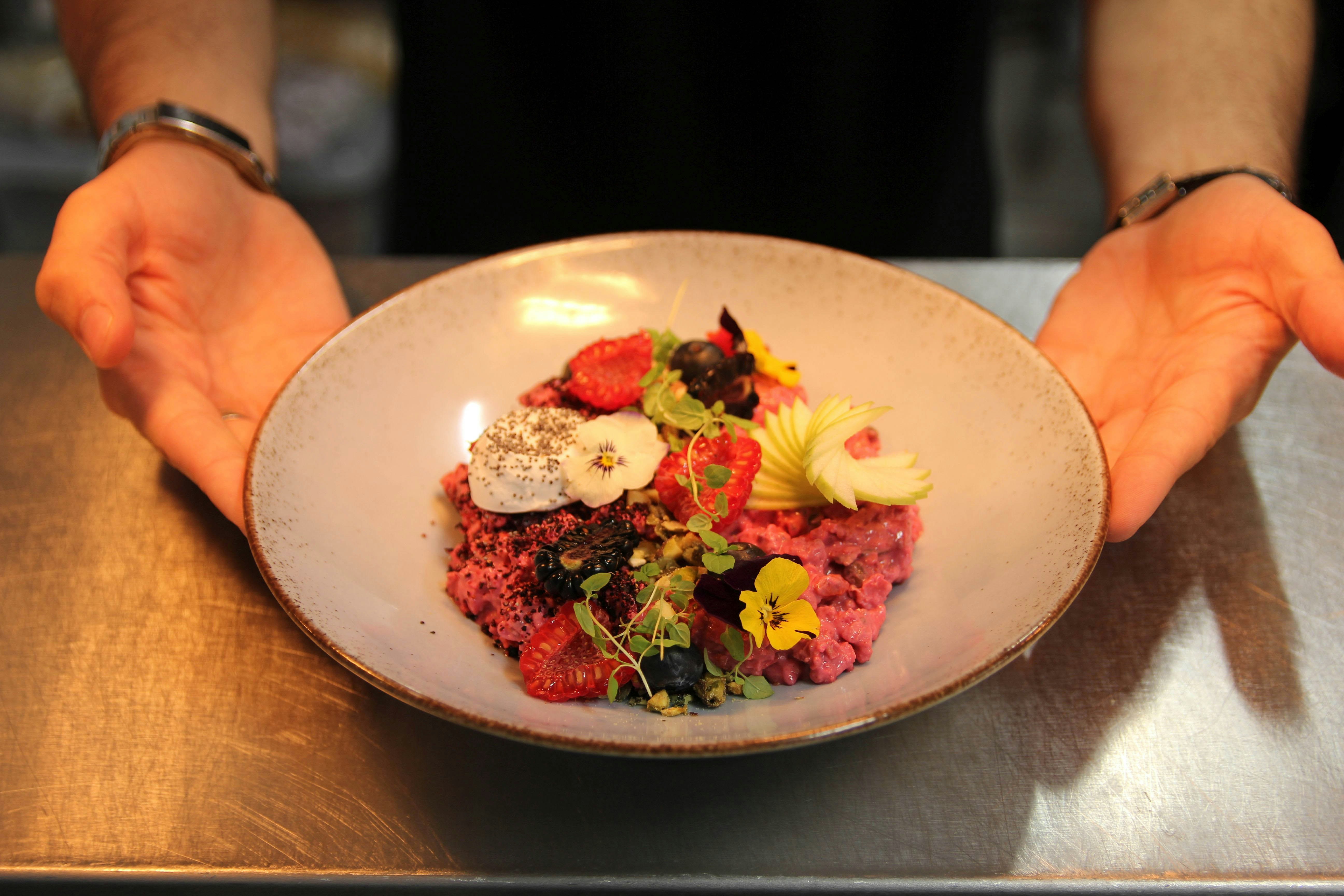A pink oat dish topped with flowers and raspberries in a shallow, pale-blue ceramic bowl. Served at EL&N, London. 