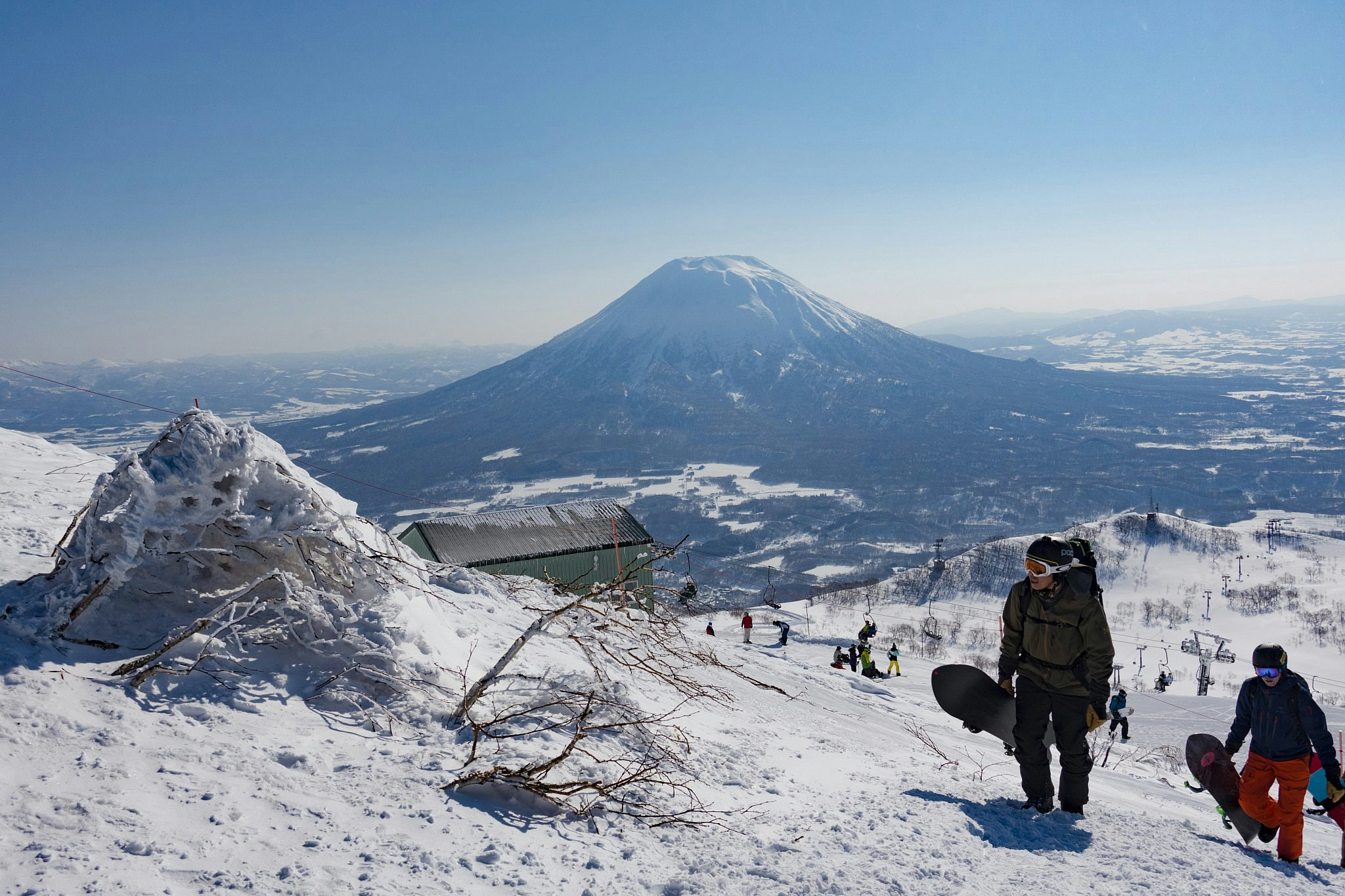 Snowboarders hike up a trail at Niseko ski resort on Mt Annupuri, Hokkaido, with another snow-covered mountain in the distance.