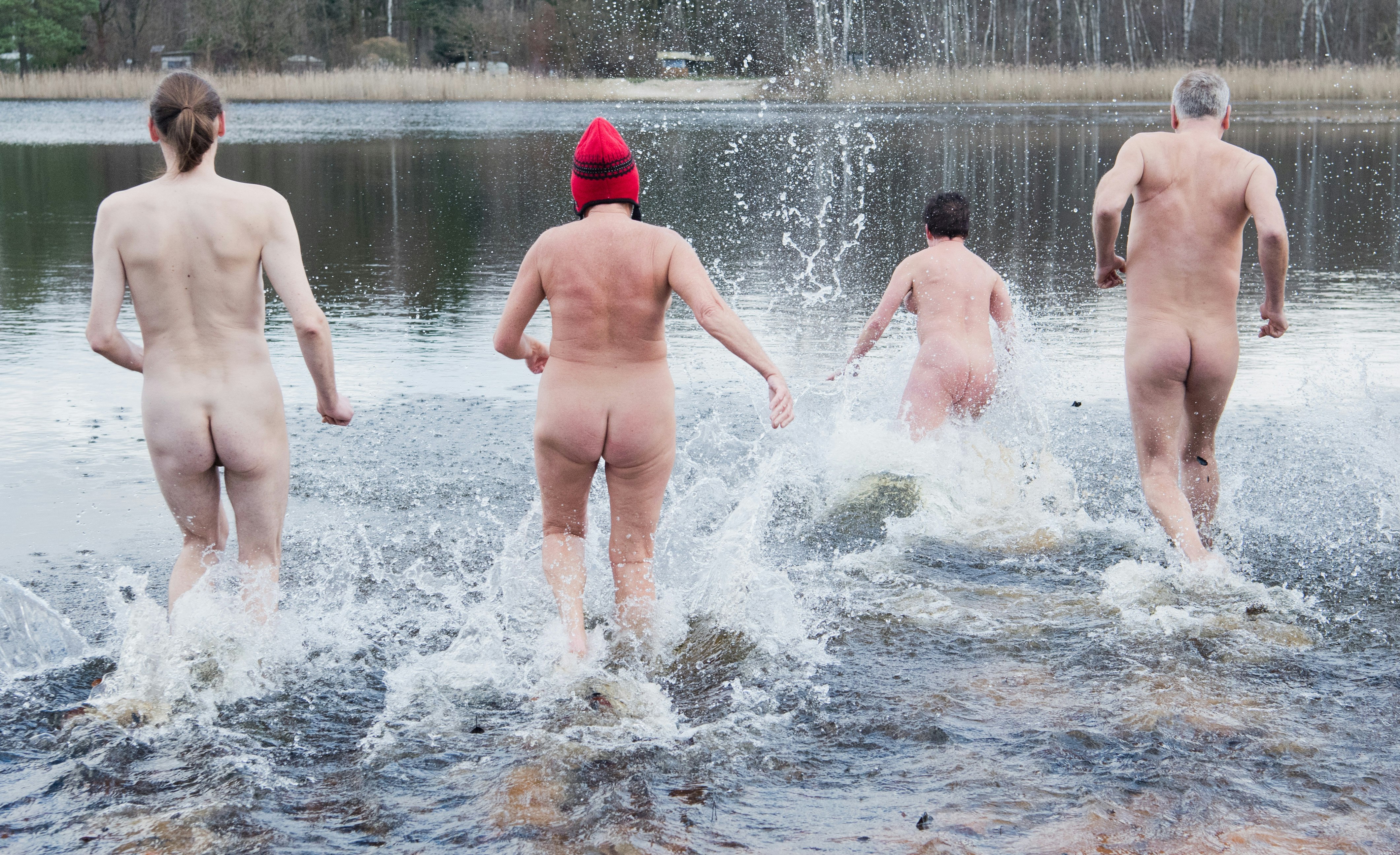 A group of people run into the cold waters in the nude in Hanover Germany. One person is wearing a red wool hat. 