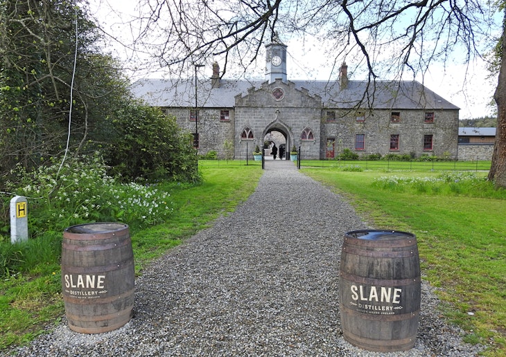 A gravel path flanked by a pair of barrels at the beginning of the path leads to an old stone building