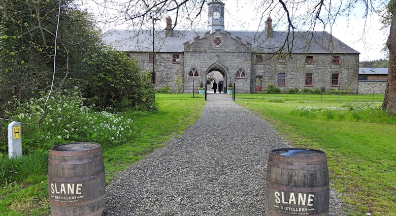 A gravel path flanked by a pair of barrels at the beginning of the path leads to an old stone building