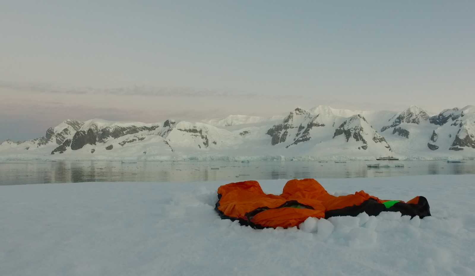 Two sleeping bags stretched out in the snow facing an ocean filled with Ice Bergs