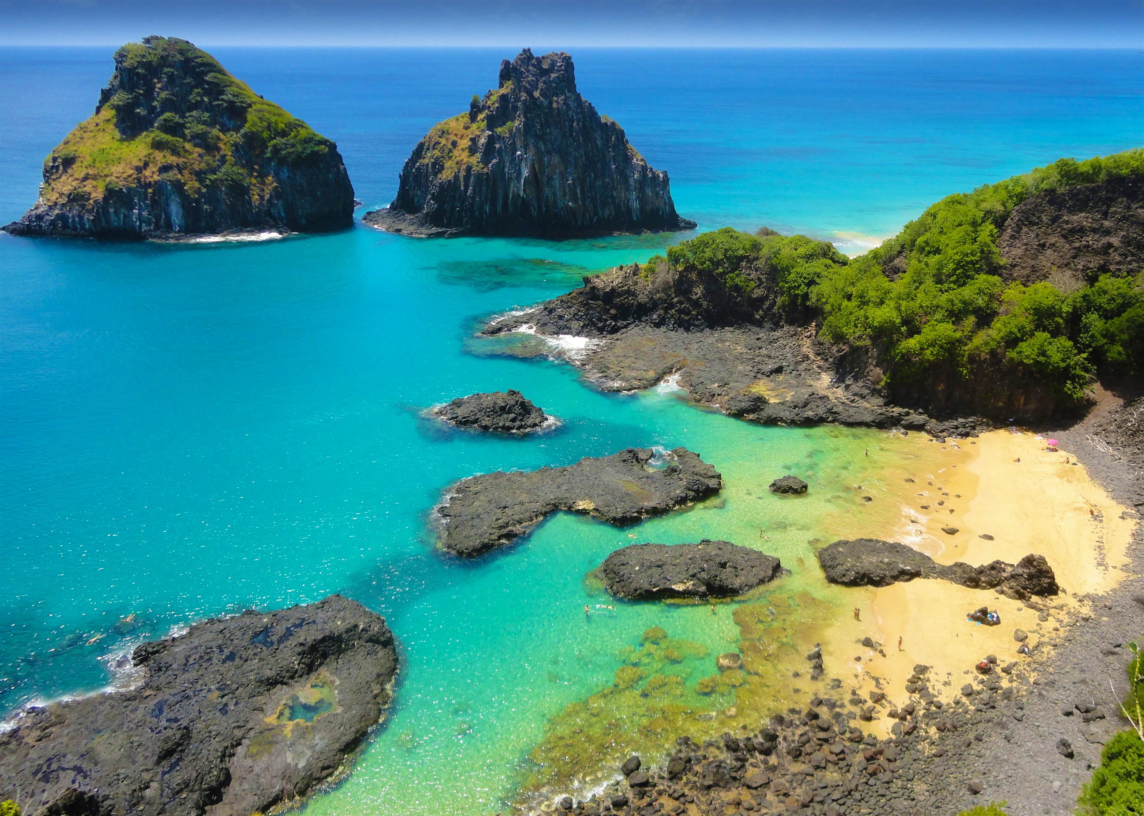 Baia dos Porcos, Brazil An aerial view of Baia dos Porcos in the Fernando de Noronha archipelago of Brazil. The water is shallow and turquoise and laps at a small white-sand beach. The water is so clear you can see to the bottom.