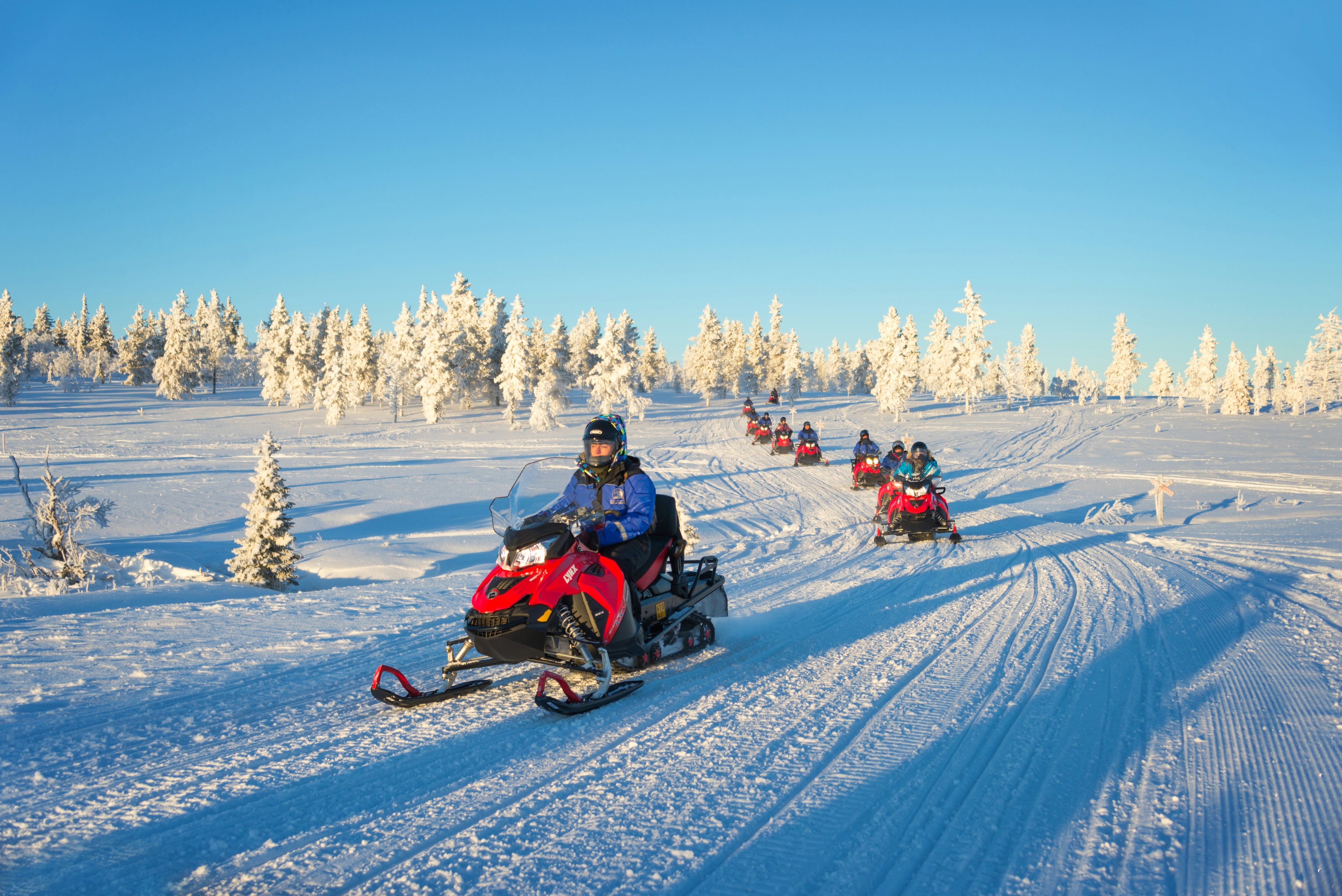 A trail of snowmobiles riding single file through a white snowscape
