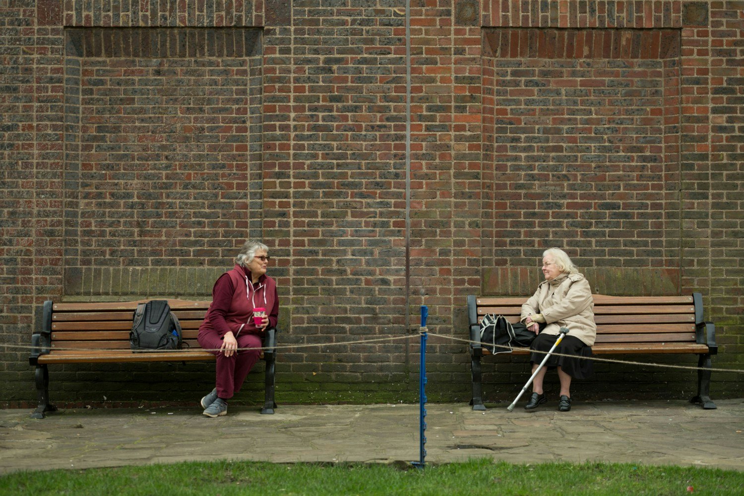Two elderly women sitting on benches practising social distancing.