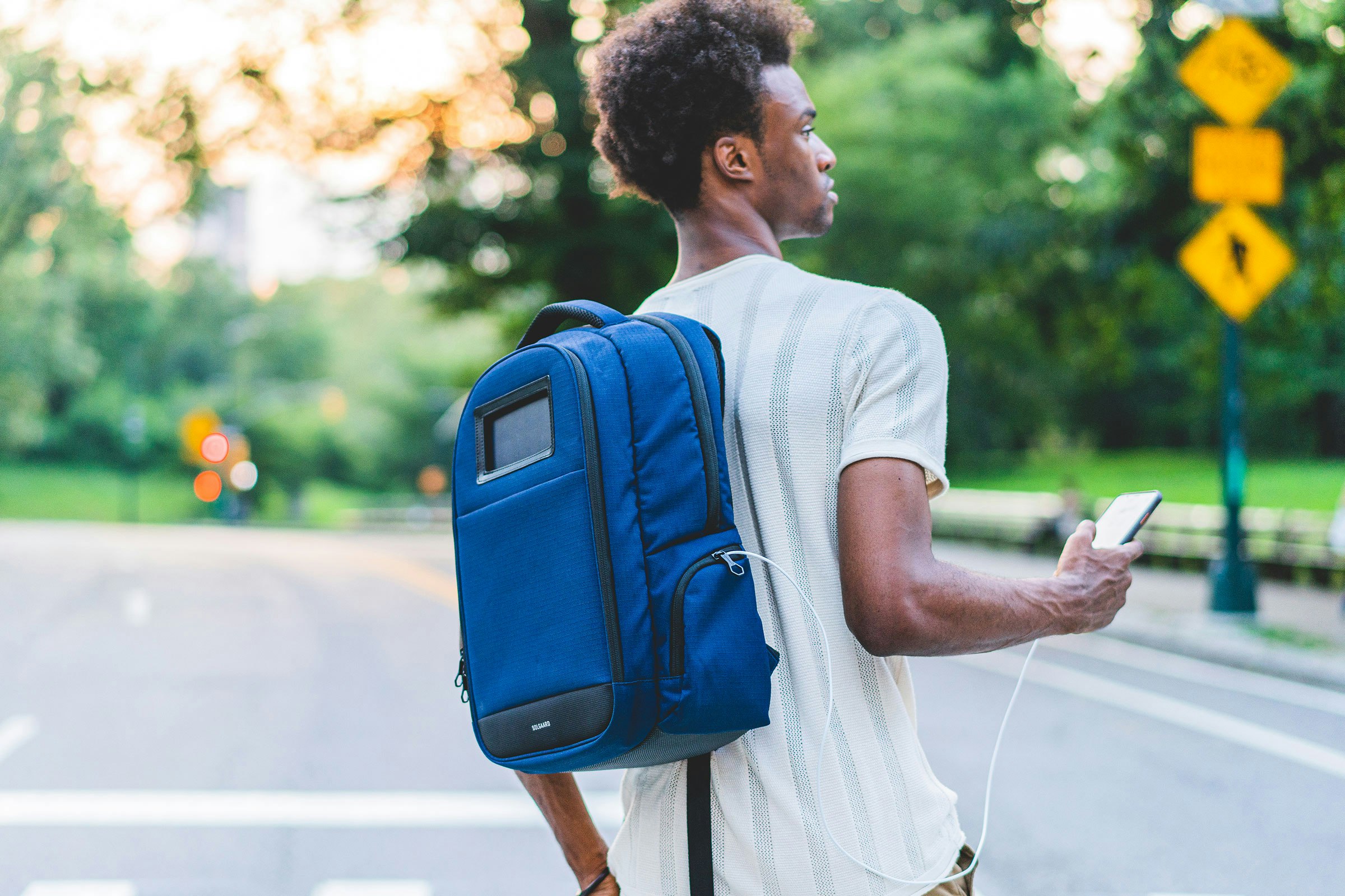 A man wearing a blue Shore-Tex Lifepack, charging his phone via a cable from the bag