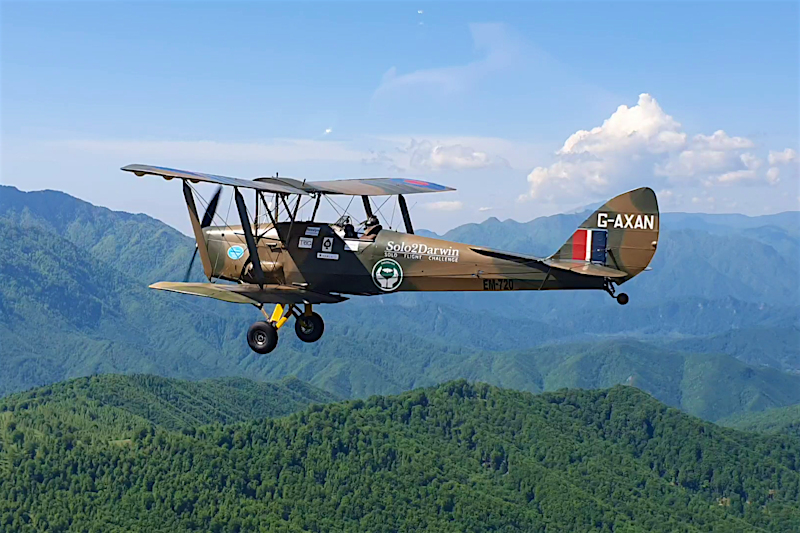 Solo2Darwin A Tiger Moth plane with 'Solo2Darwin' on the side flies over lush green hillsides