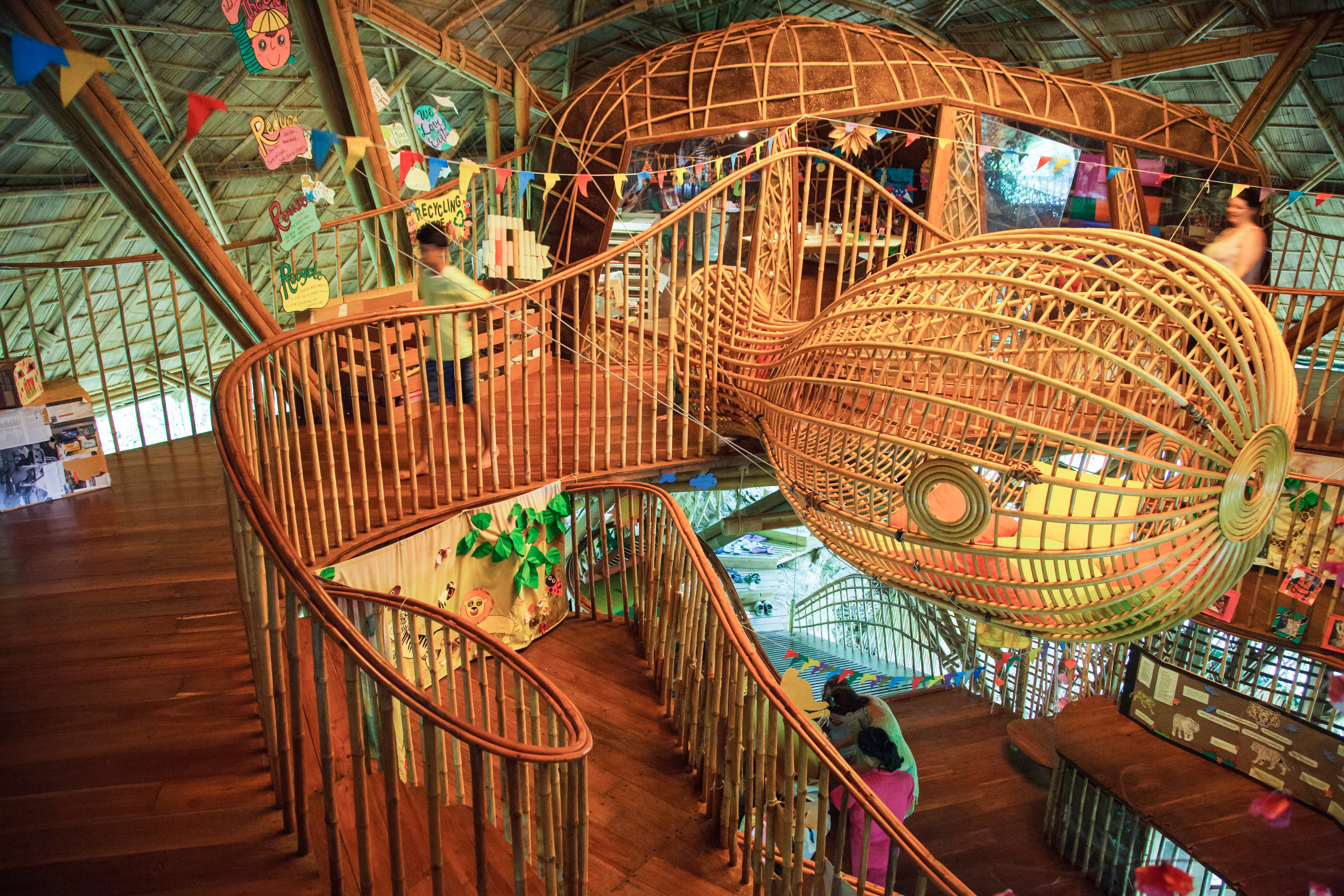 A bamboo structure is fashioned in the shape of a mantra ray; a boy is playing on a platform next to it. Winding stairs lead to the floor below.