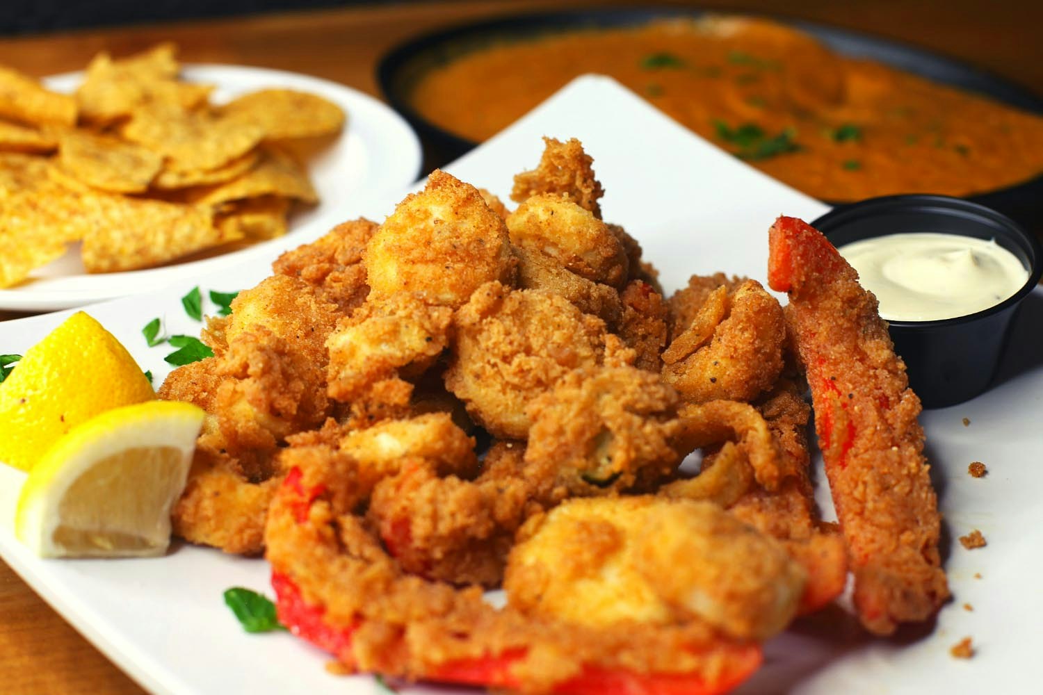 Closeup of a plate of seitan fried 'chicken' with a side of fried red peppers. In the background is a plate of chips and dip; San Francisco Bay Area vegan restaurant 