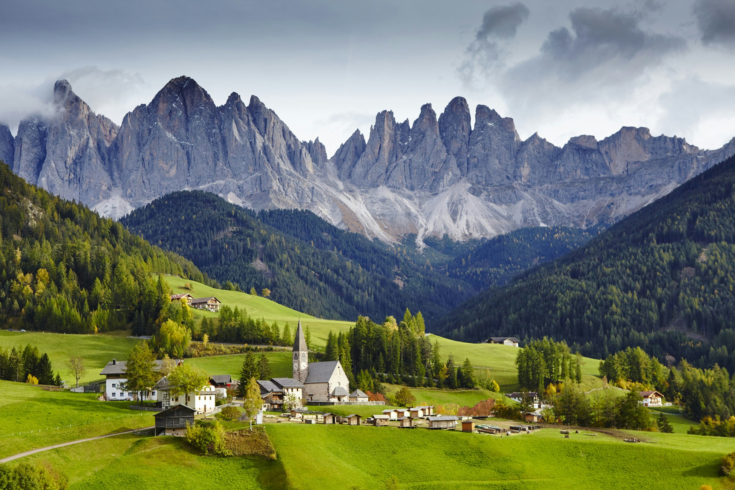 Jagged peaks form a backdrop to a church and farmhouses set in green meadows