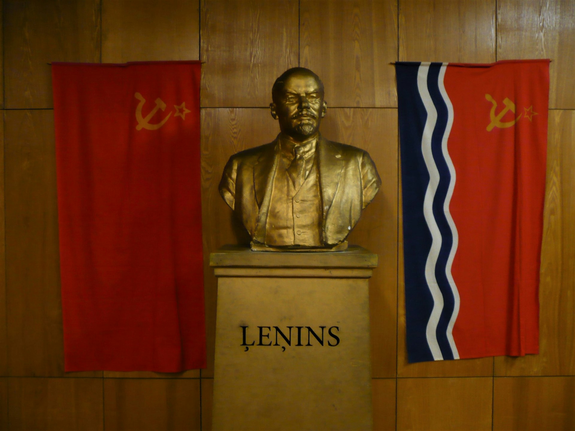 A bust of Lenin stands between two Soviet flags